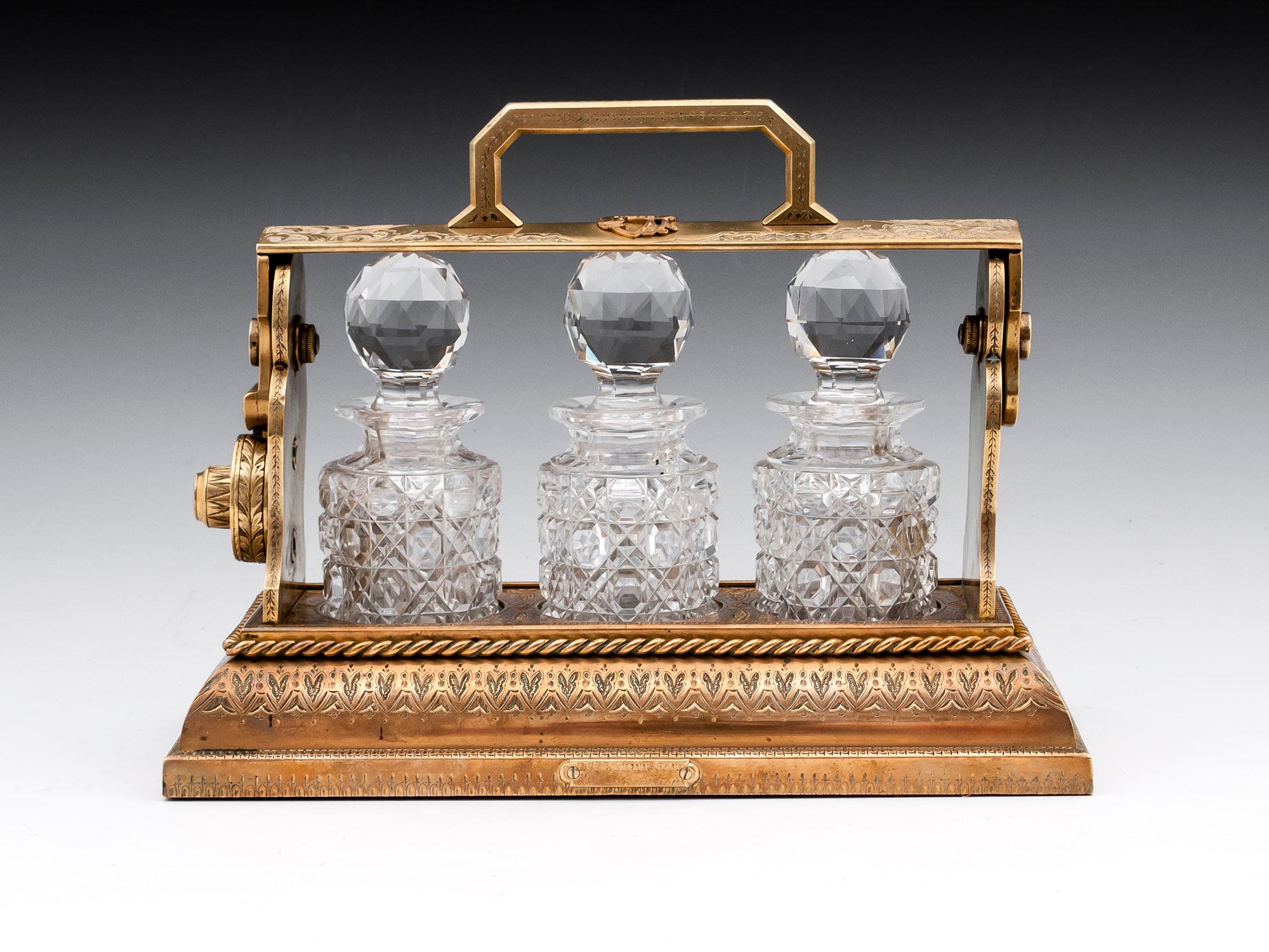 Bronze engraved and gilded miniature Tantalus by Betjemann. With three hobnail cut-glass bottles with faceted stoppers. The handle has a raised monogram 
