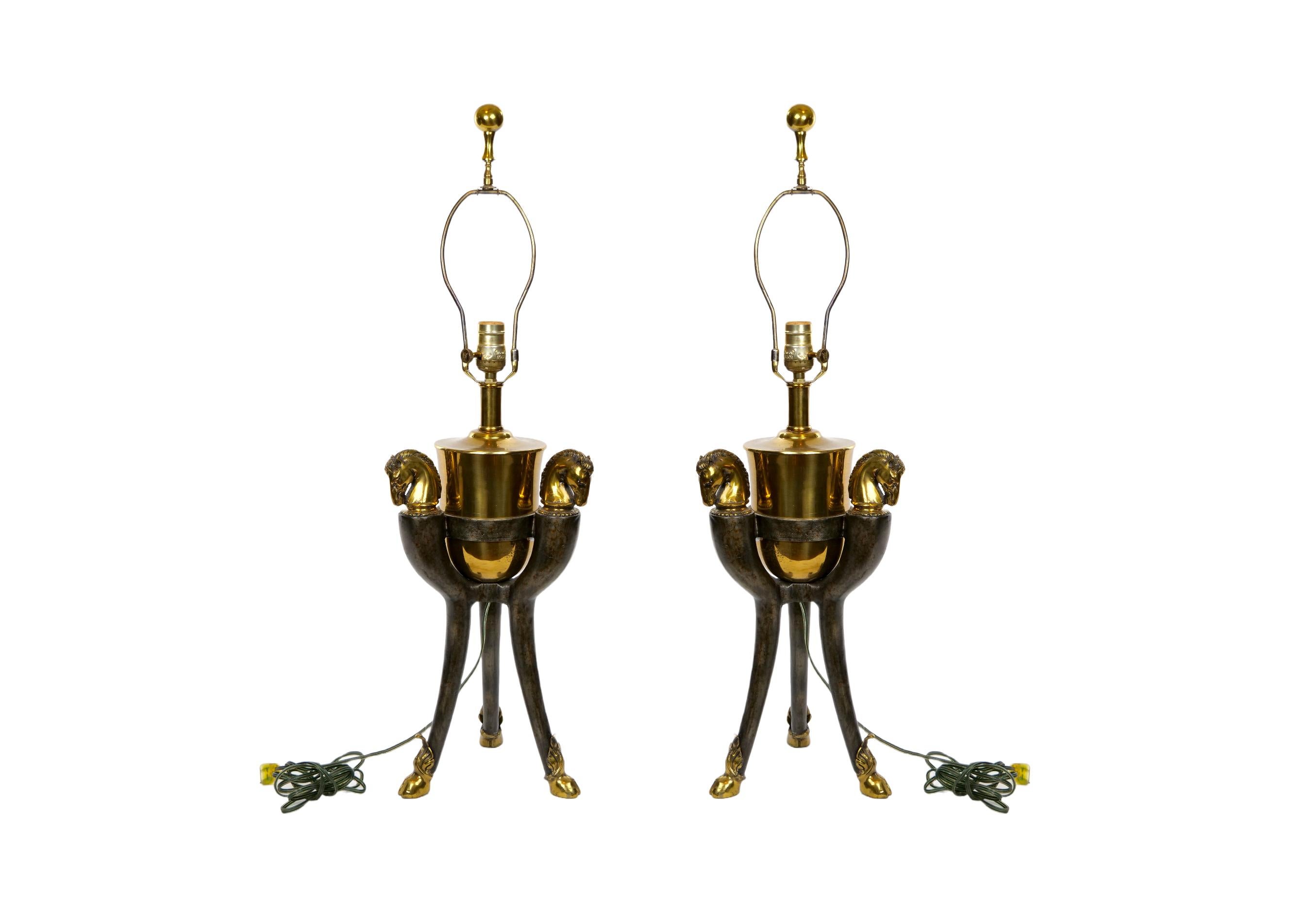 Late 20th century bronze and gilt brass  horse head sculpture pair decorative table lamps. Each lamp features a gilt brass top with three horses head details resting on three feet gilt with horse shoes design. Each lamp is in good working condition.