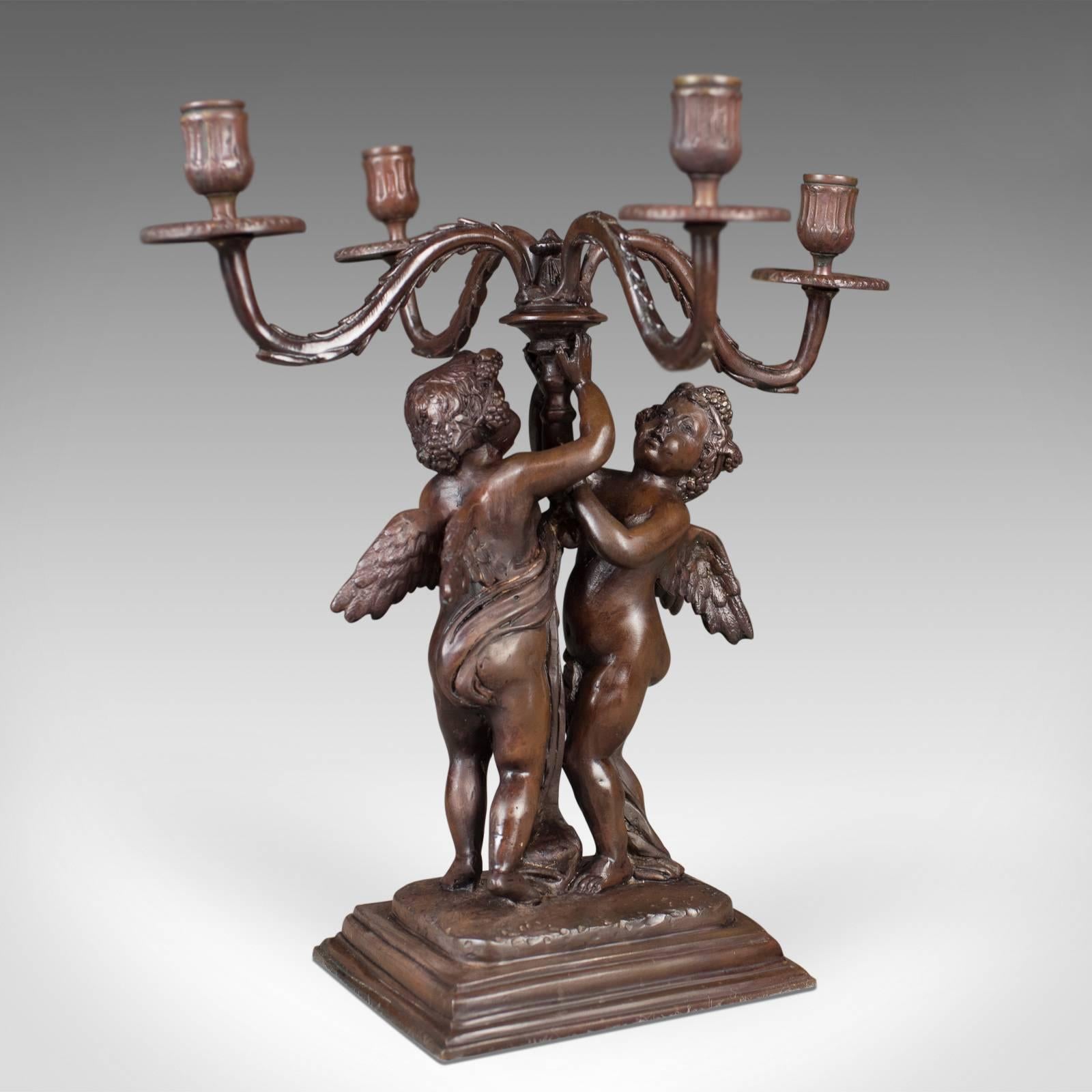This is an attractive bronze girandole candelabra, a four branch Victorian revival candlestick dating to the mid-20th century, circa 1960.

Raised on a stepped plinth base
A pair of winged cherubs elevate the girandole
Four sinuous branches
