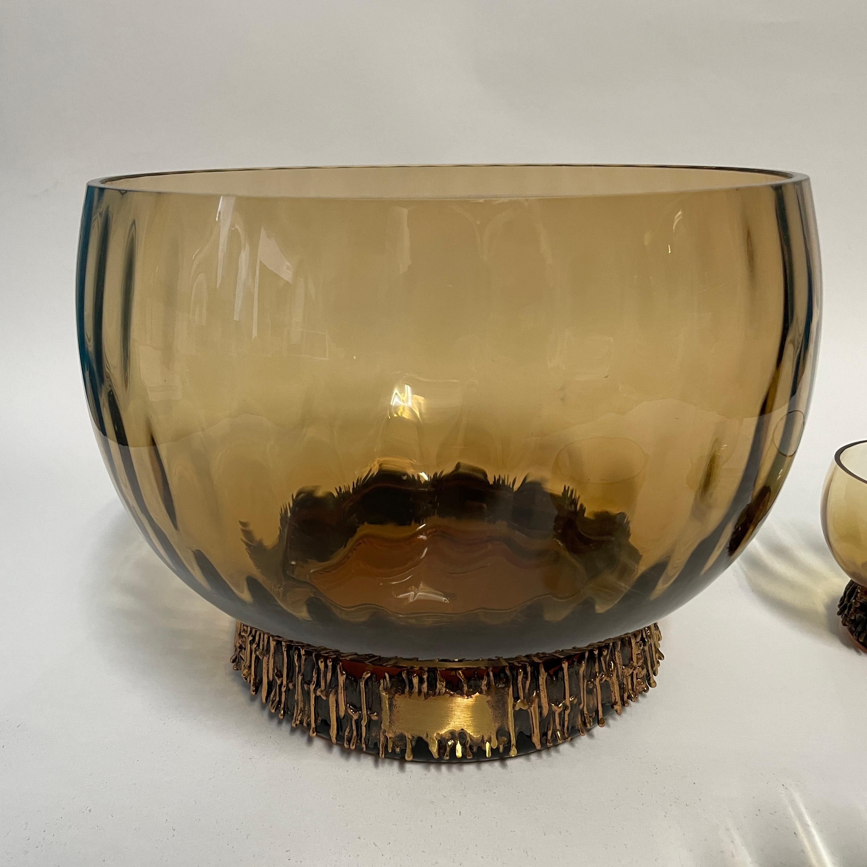 Le vase et les verres à punch Kaarna de Kumela ont été conçus par Pentti Sarpaneva et fabriqués dans les années 1960. S'élevant sur un cerceau de bronze, le verre impressionne par son magnifique design rond et organique. 
Les détails de l'arceau en