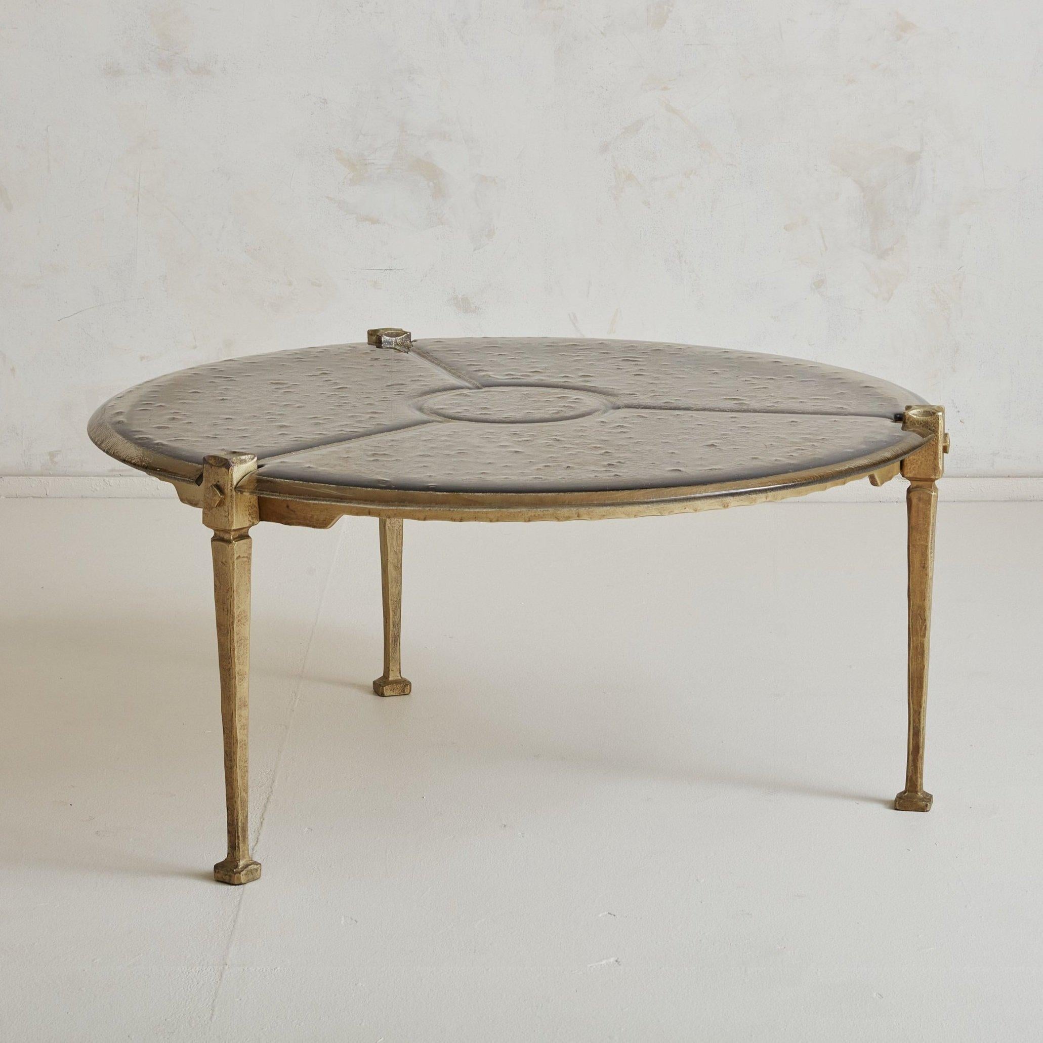 A rare brutalist bronze and glass top round coffee table by German designer Lothar Klute. This coffee table features a forged bronze frame with three tapered legs, textured bubble glass top, and square bronze feet. A gorgeous geometric design in