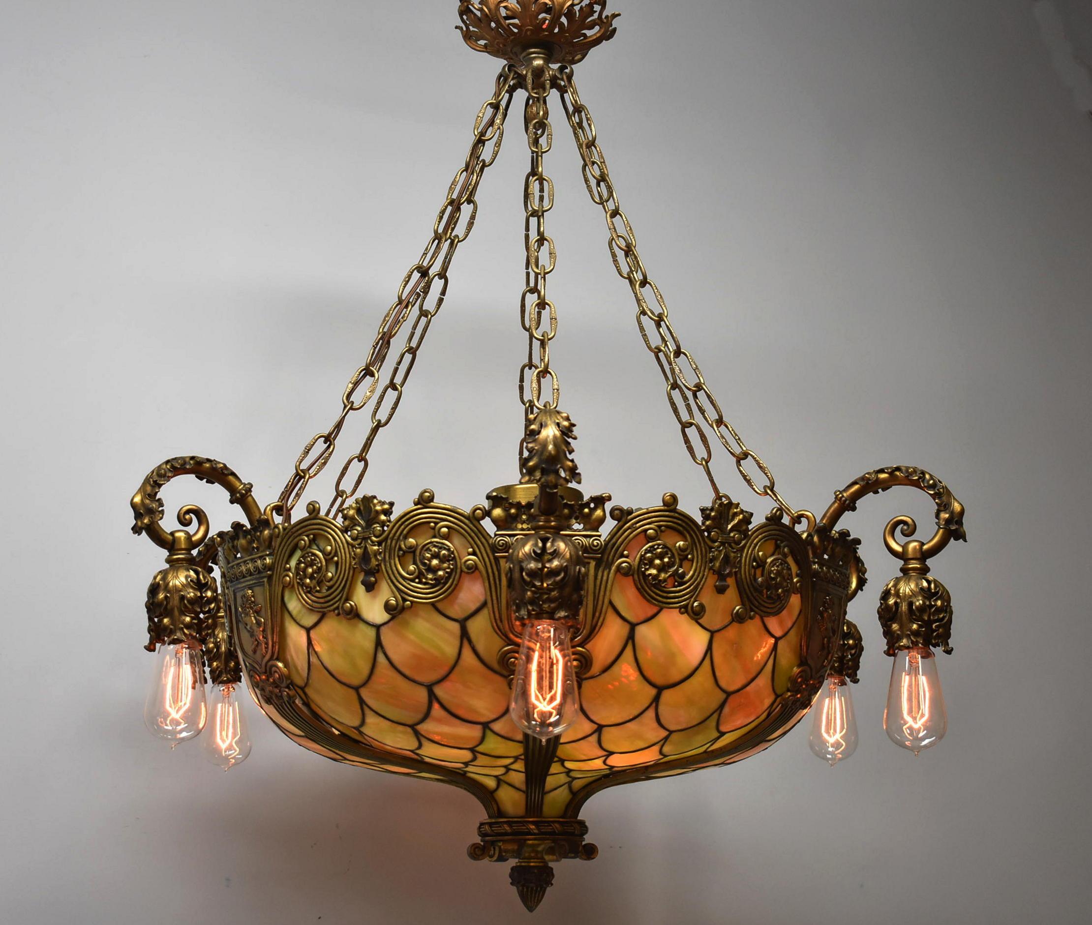 Antique bronze Gothic Revival fish scale leaded glass chandelier. Inverted bronze dome with bronze overlay. Six ribbed segmented frame with lion shield details around the top. Six original ornate exterior sockets and six original interior sockets.