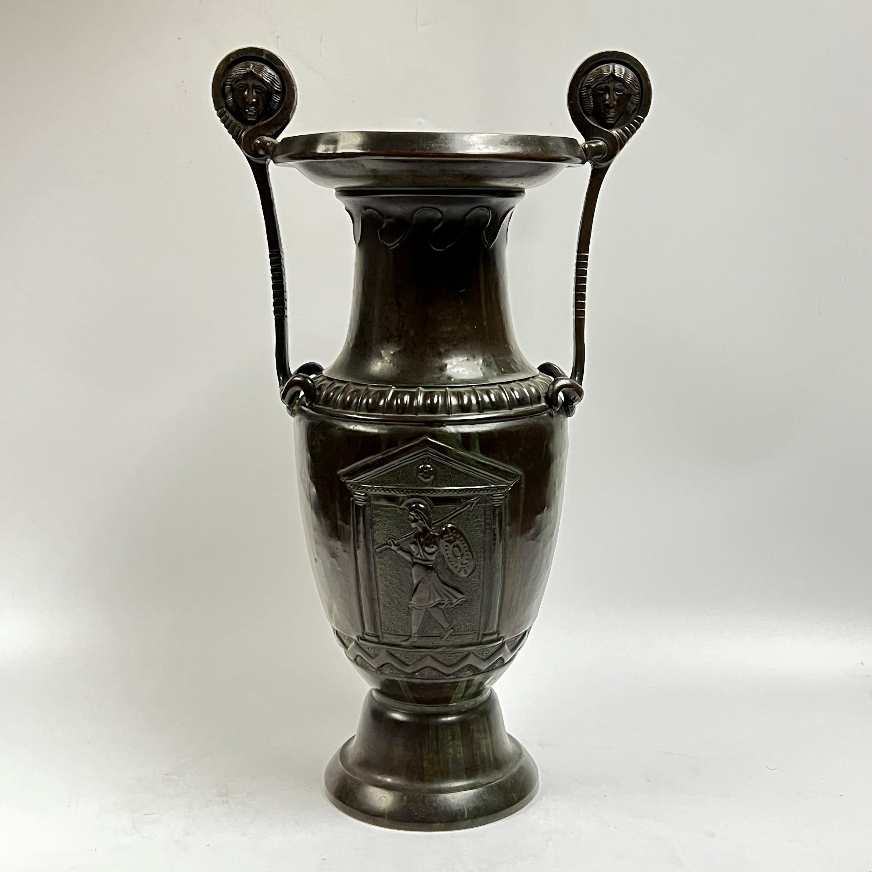 Cratere greco a volute in bronzo patinato con cartigli raffiguranti soldati armati e manici raffiguranti maschere.