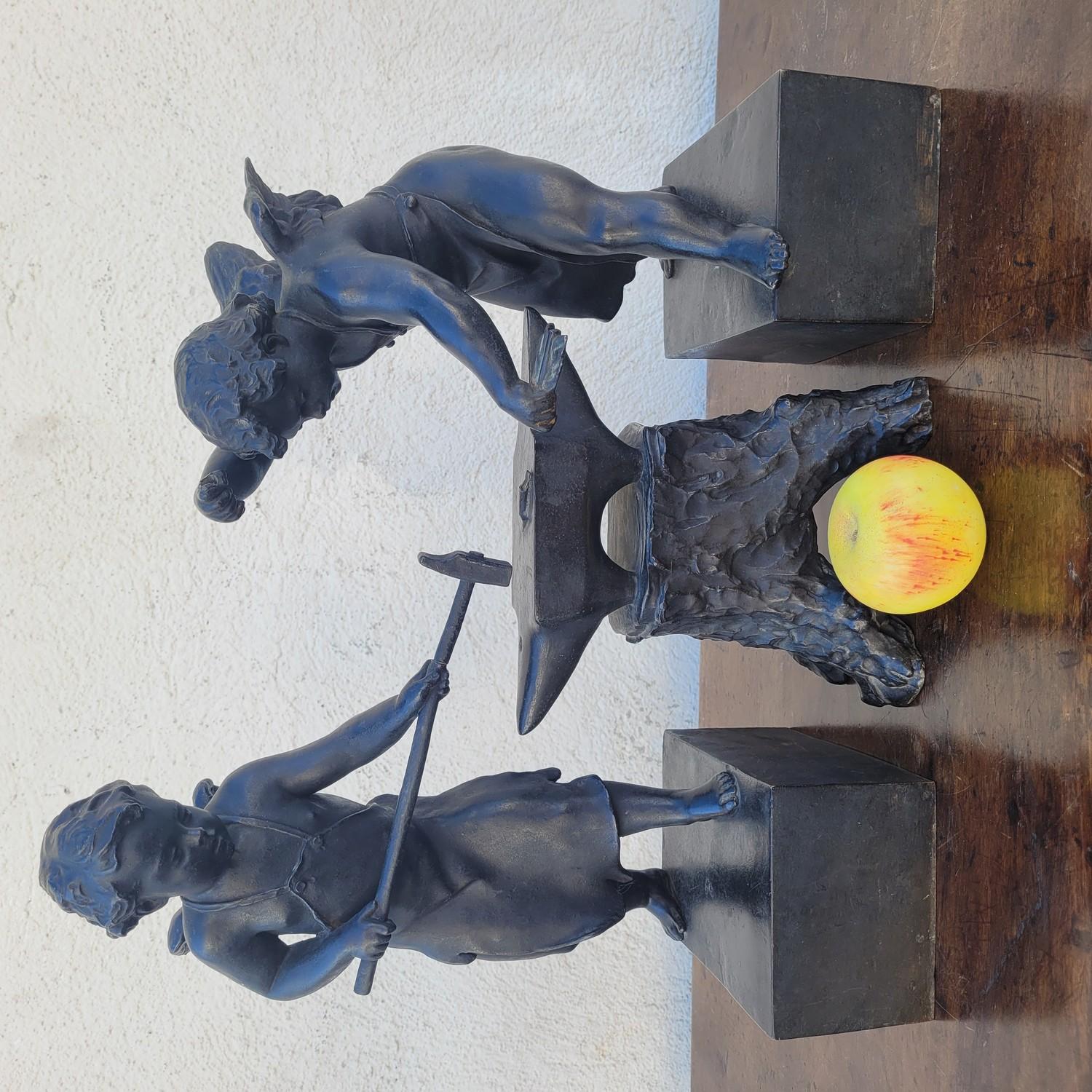 Bronzegruppe mit brauner Patina, bestehend aus 3 Skulpturen: 2 Schmiedeputti schmieden ihre Pfeile auf einem Amboss.   

Abnutzung, fehlende Teile (Werkzeuge) und alte Restaurierungen (Hammer).   

Bronzeskulpturen des 19. Jahrhunderts.  
