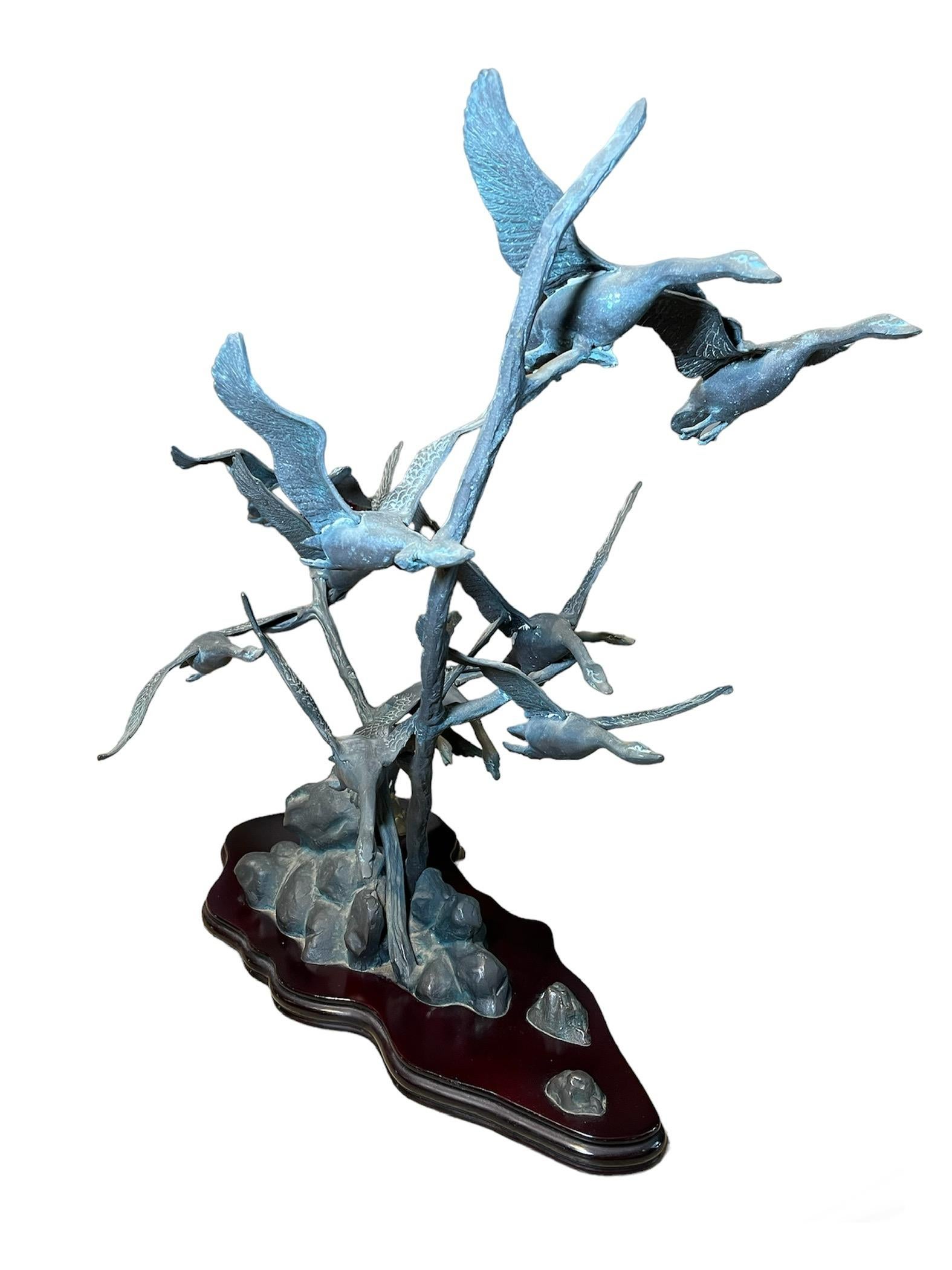 This is a Bronze Group Sculpture of Gulls. It depicts a large bronze sculpture of a group of gulls emigrating over the sea while another one is standing over some rocks. The sculpture is supported by an asymmetrical large triangular wood base. It is