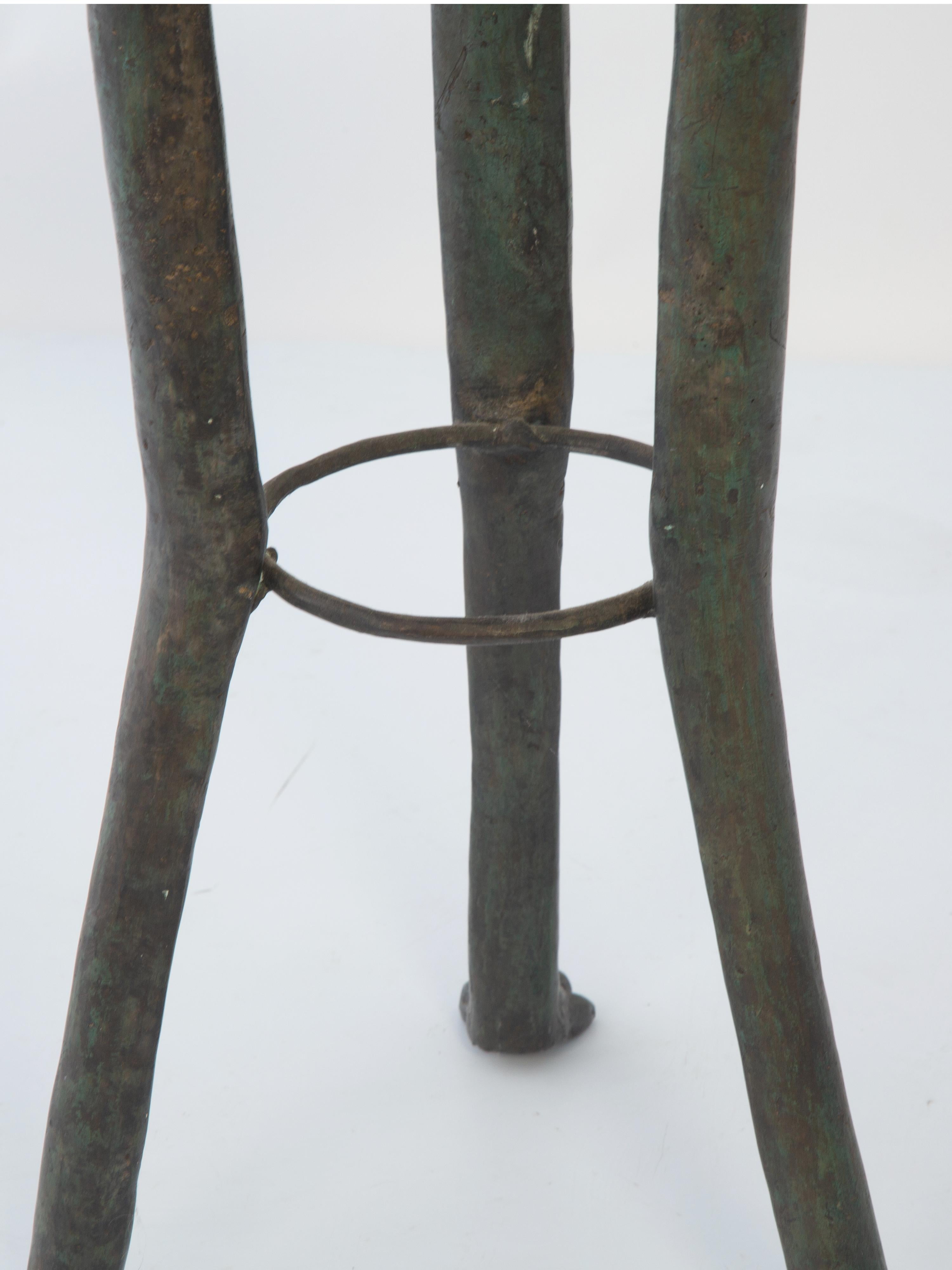 Gueridon side table or stand, having a round top of Calcutta marble. Raised on a base of hammered bronze with a patinated finish. Raised on a trio of splayed legs, each headed by elephant masks with rings, and ending in paw feet, joined by a
