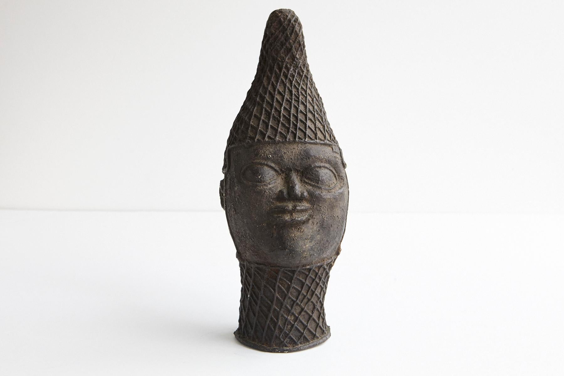 A Benin bronze of an Oba. Oba means ruler in the Yoruba language.
Wearing a lattice-pattern cap with strands of beads suspended around the head.
The neck is bound with a lattice-pattern tight choker.
The head represents the character and destiny of