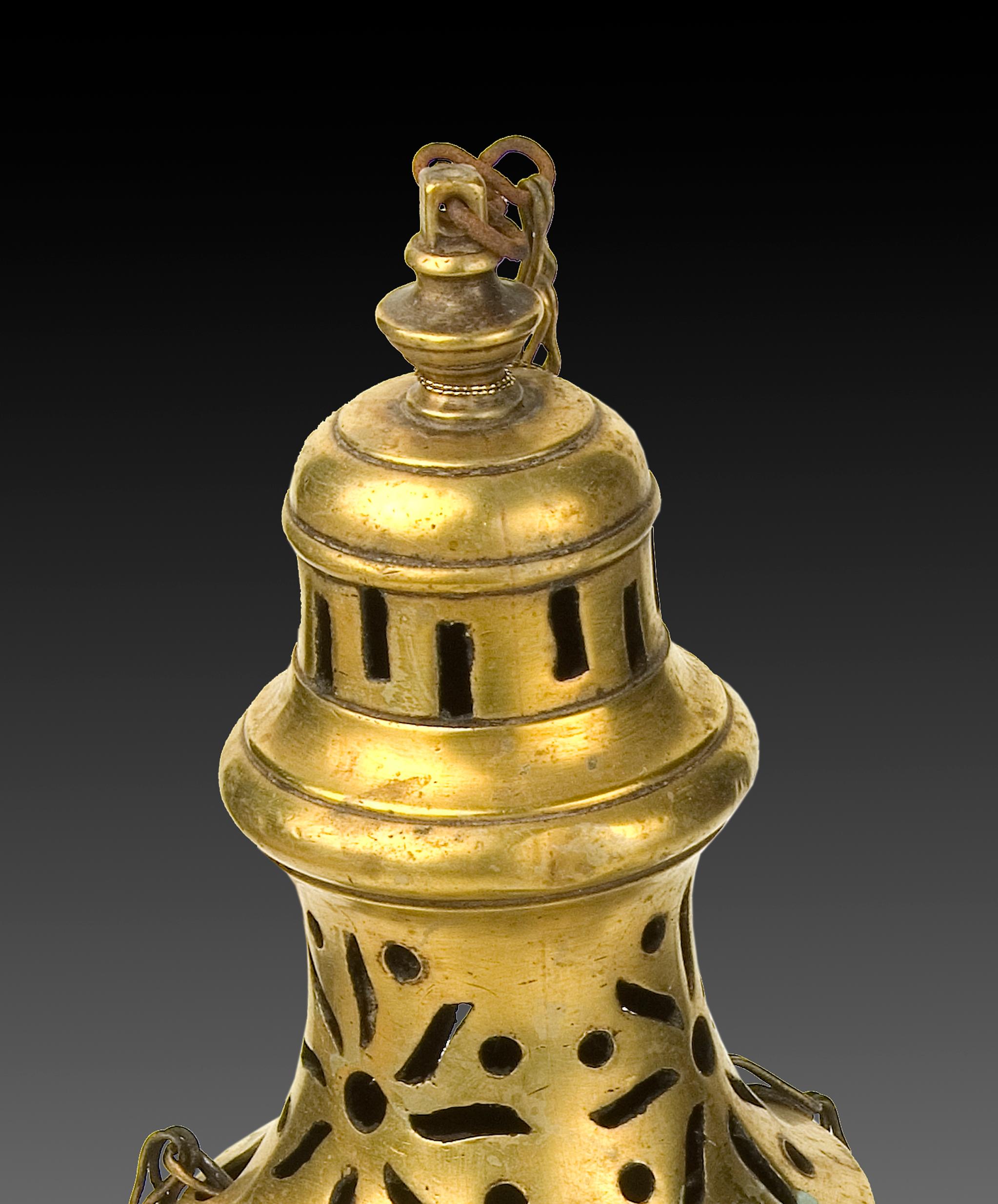 Censer. Bronze. XIX century. 
Bronze censer with circular base and cup shape with lid of elaborate lines and simple openwork elements inspired by antique pieces. It has metallic chains that join it to the usual piece with ring. Certain lines and