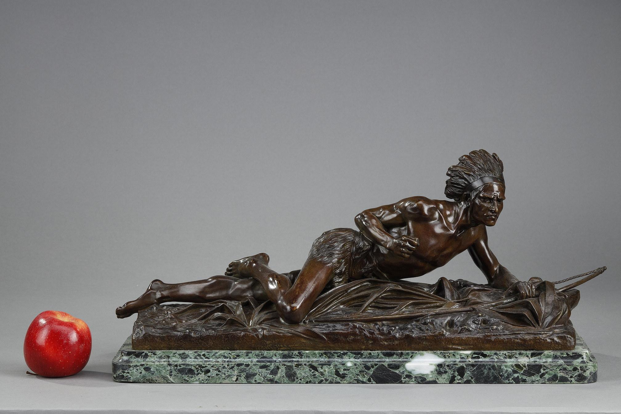 Bronze sculpture of a native American in brown and green patina after Edouard Drouot. It represents a long-haired native American dressed in a hairy loincloth and a feathered headdress lying on the ground. His distant gaze seems focused as he closes