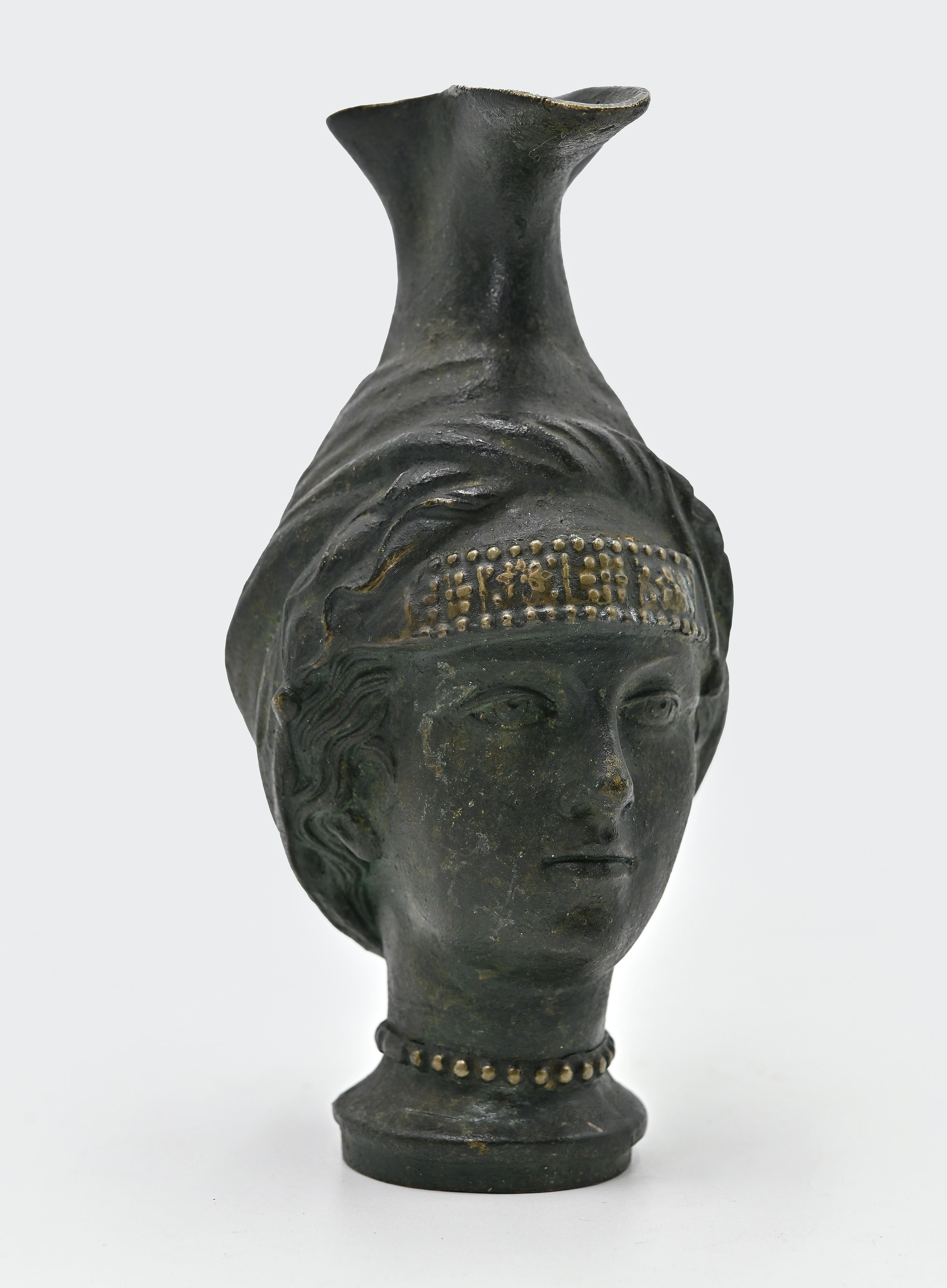 La jarra de bronce es un objeto original realizado por un artista anónimo a principios del siglo XX.

Jarra realizada a la manera antigua, con forma de cabeza femenina, con pico y base redonda.

Fundición de bronce con verdigris. 

¡No te