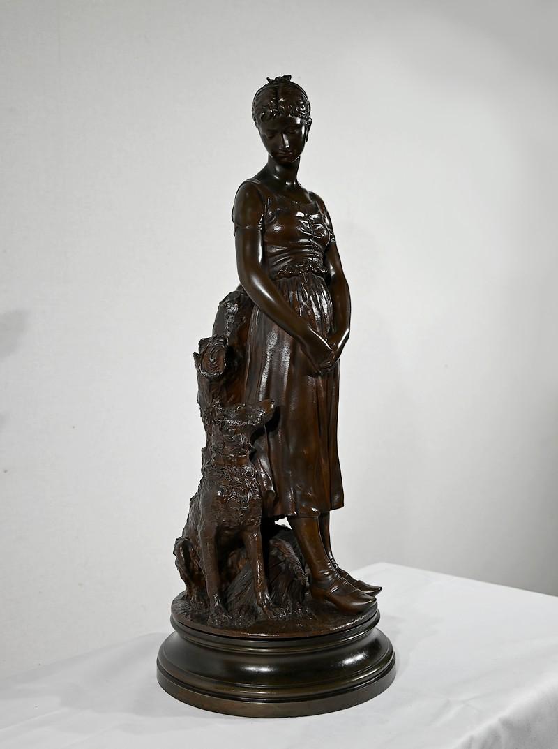 Elegant bronze sculpture with a brown patina by Truffot.
This work depicts a woman standing with clasped hands beside her dog. She is wearing a long dress and leaning against a tree trunk. Her companion, seated beside her, stares at her.
The base,