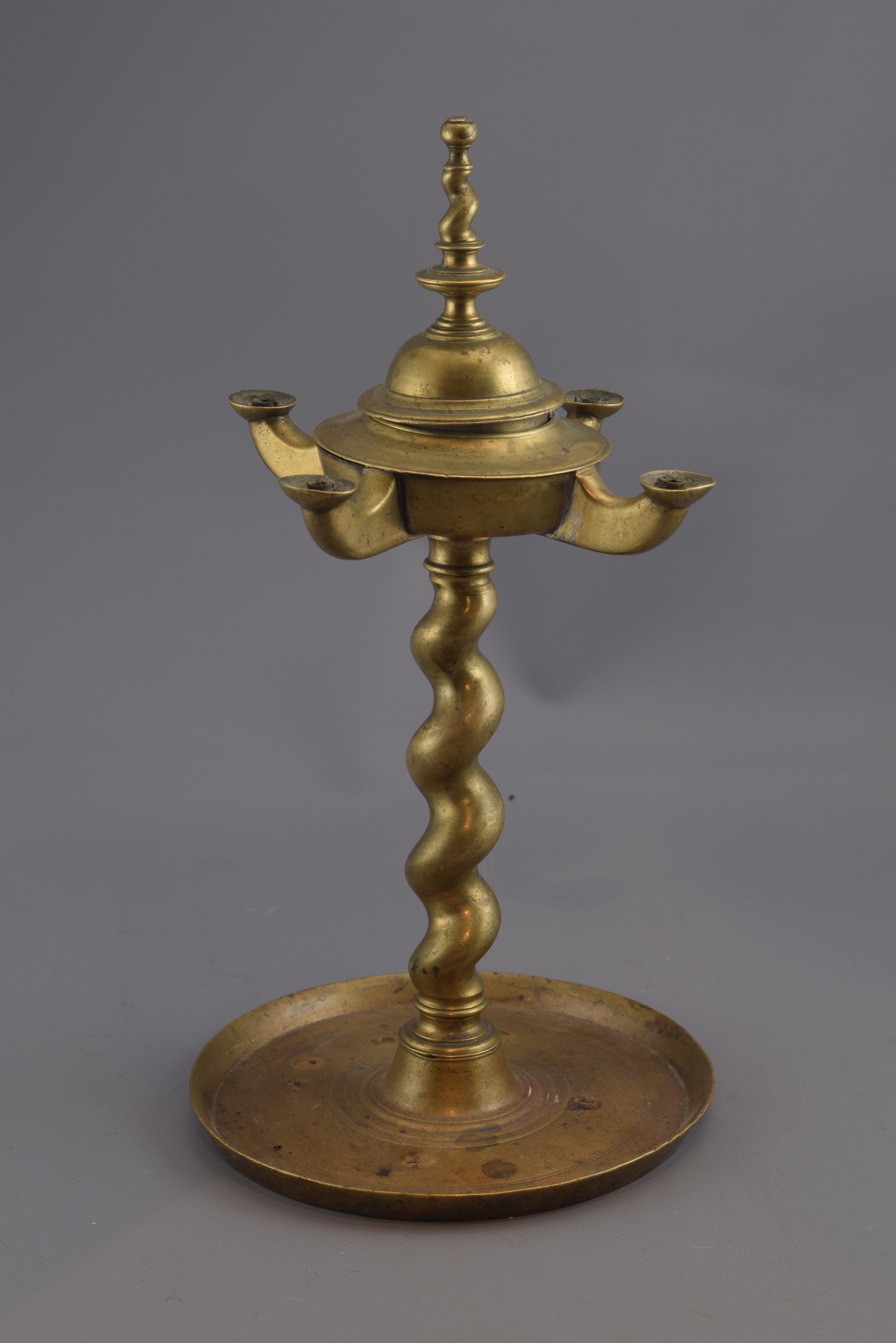 Oil table lamp made entirely of bronze, composed of a circular base decorated with concentric lines, a salomonic foot that is continued at the top of the piece and the container for the oil at the top, which has four points of light. The influence