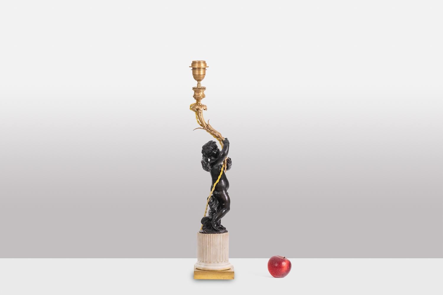 Lamp representing a winged putti in bronze, resting on its marble base composed of a fluted shaft, or rudenté, and holding an arm of light in gilded bronze ending in the upper part with a bobèche.

French work realized circa 1880.

Dimensions: H 56