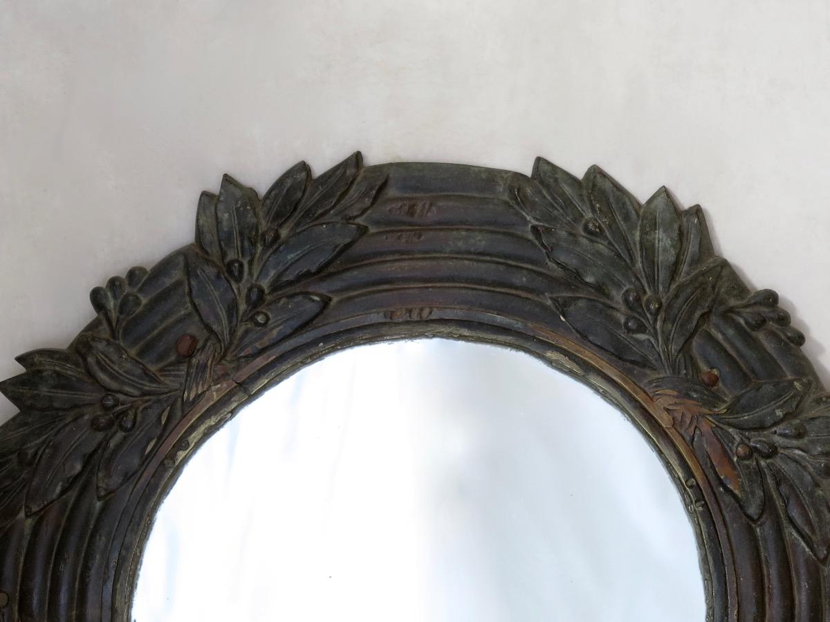 Round mirror with a solid bronze, reeded frame, adorned with motifs of laurel wreaths. There are a couple of small holes in the frame to fix it to a wall. Antique mirror.