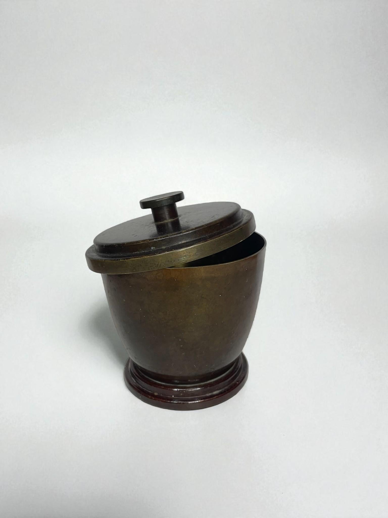 Élégante jarre à couvercle en bronze produite par Ildfast au Danemark dans les années 1930. La pièce présente une forme lisse et arrondie avec un couvercle ajusté et une poignée à bouton, reposant sur une base circulaire étagée.

La surface présente