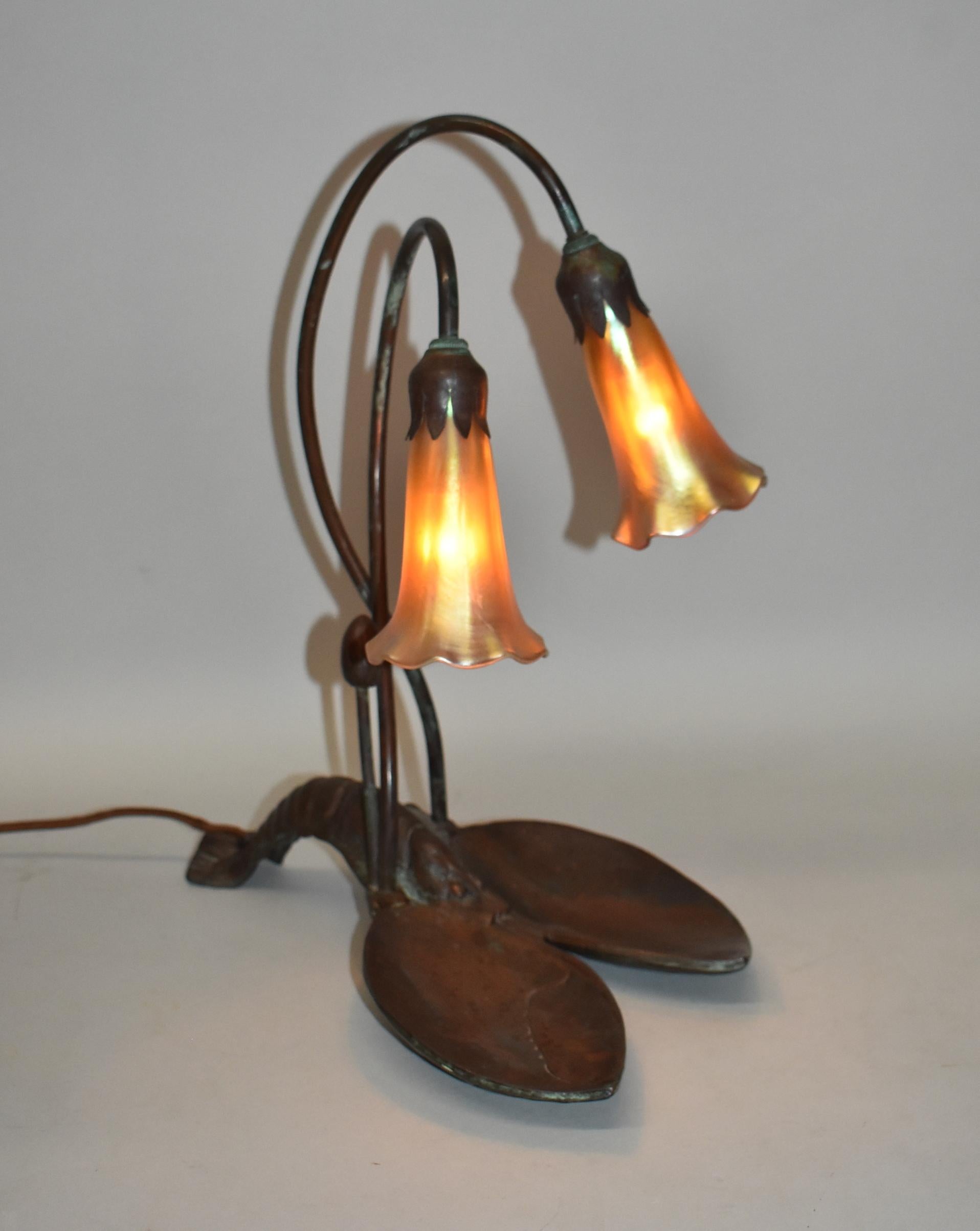 Whimsical art deco lamp with a bronze lobster base and tulip shades. The lobster base has 2 cupped areas for the claws and an arched tail. Flower stems have sepals holding the yellow iridescent tulip art glass shades alongside one unopened bud. The