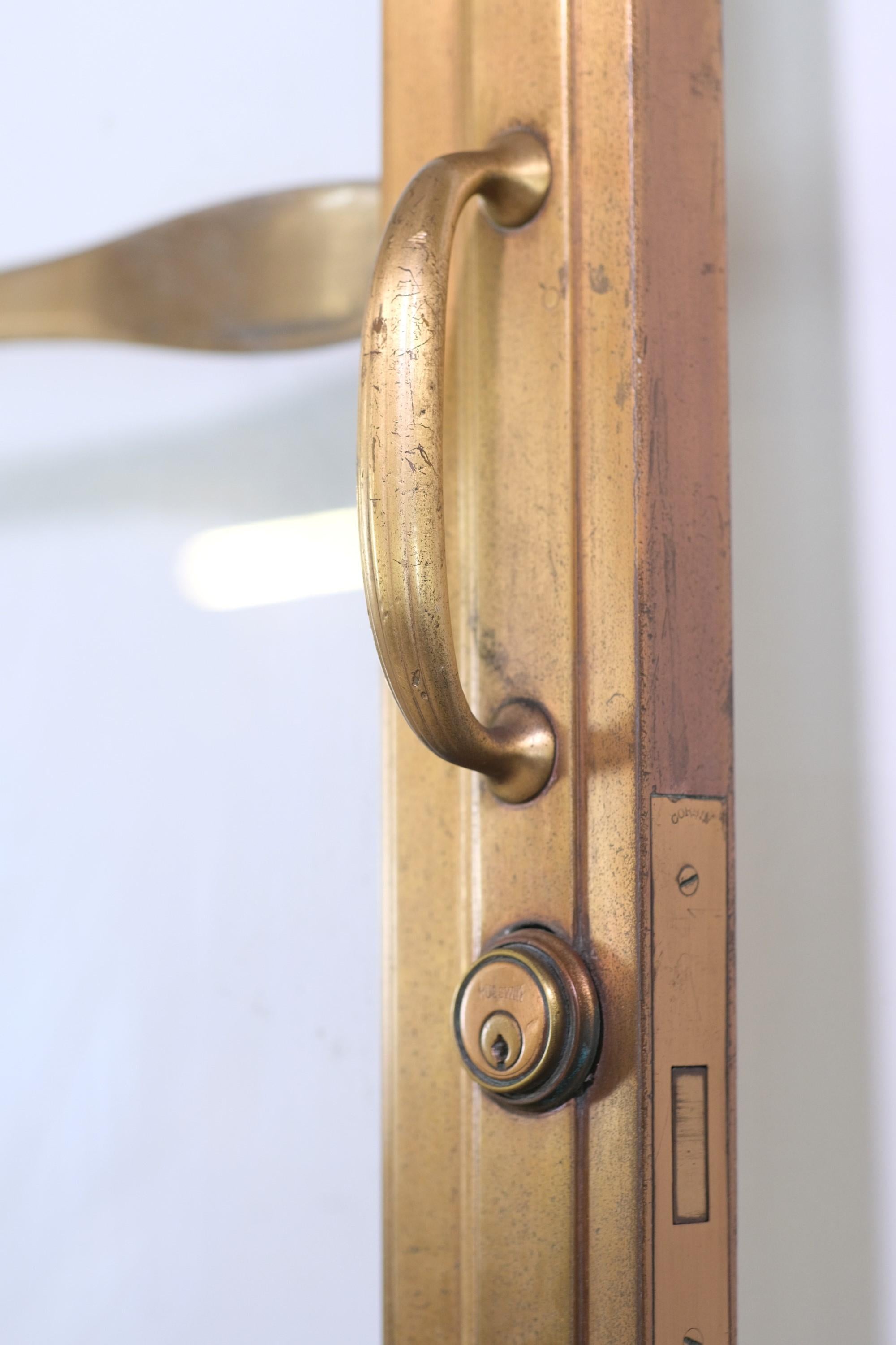 1926 Exterior bronze industrial lobby doors with one lite of glass each and the original push bars, fluted handles, and locks. One lite has a small crack. Typical scratches, small dings, etc. Please see images. Priced as a set. Measures 88.75 x 117.