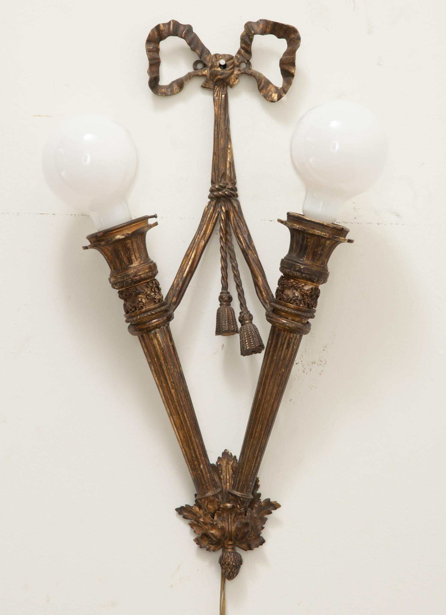 Ein französischer Wandleuchter im Louis-XVI-Stil mit zwei Glühbirnen. Diese klassisch gestaltete Bronzeleuchte zeigt einen Bogen, der sich um zwei kannelierte Säulenformen windet und mit einem Lorbeerblatt-Anhänger endet. Professionell neu
