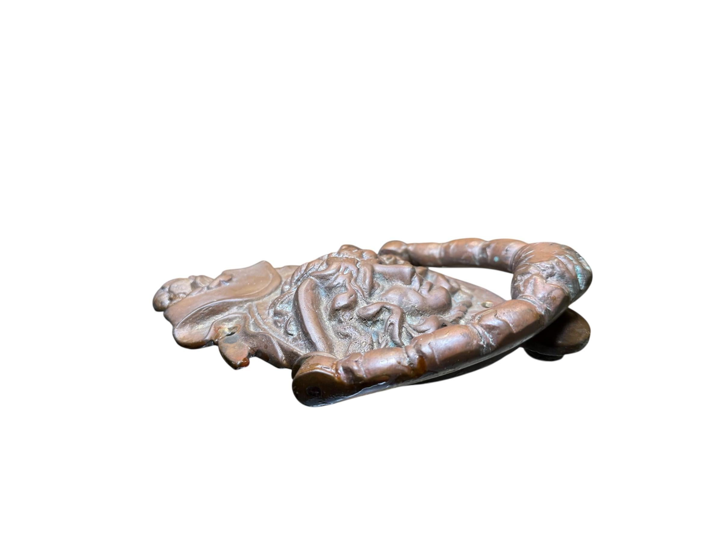 This is a Bronze Door Knocker. It depicts a patinated bronze oval door knocker with the relief of the head and face of the Medusa. The head covered with curly hair ( snakes bodies ) and some wings at each side at the top. The tails of the snakes