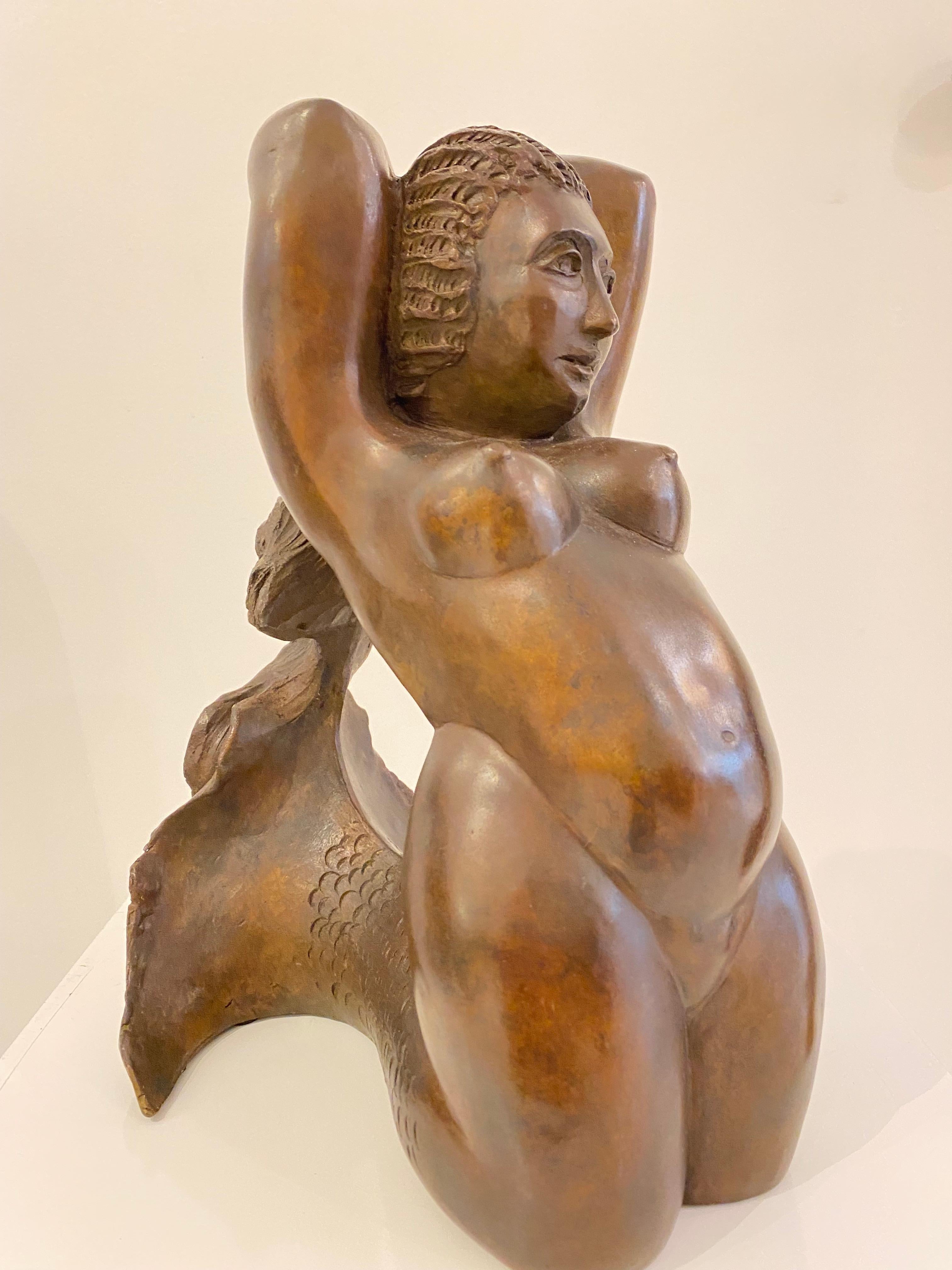 This is a beautifully patinated bronze mermaid sculpture by Barbara Beretich. The mermaid is kneeling with her arms up. Her hair seamlessly blends into her beautiful fin. the sculpture has a beautiful liver bronze finish. The fin is exquisite and