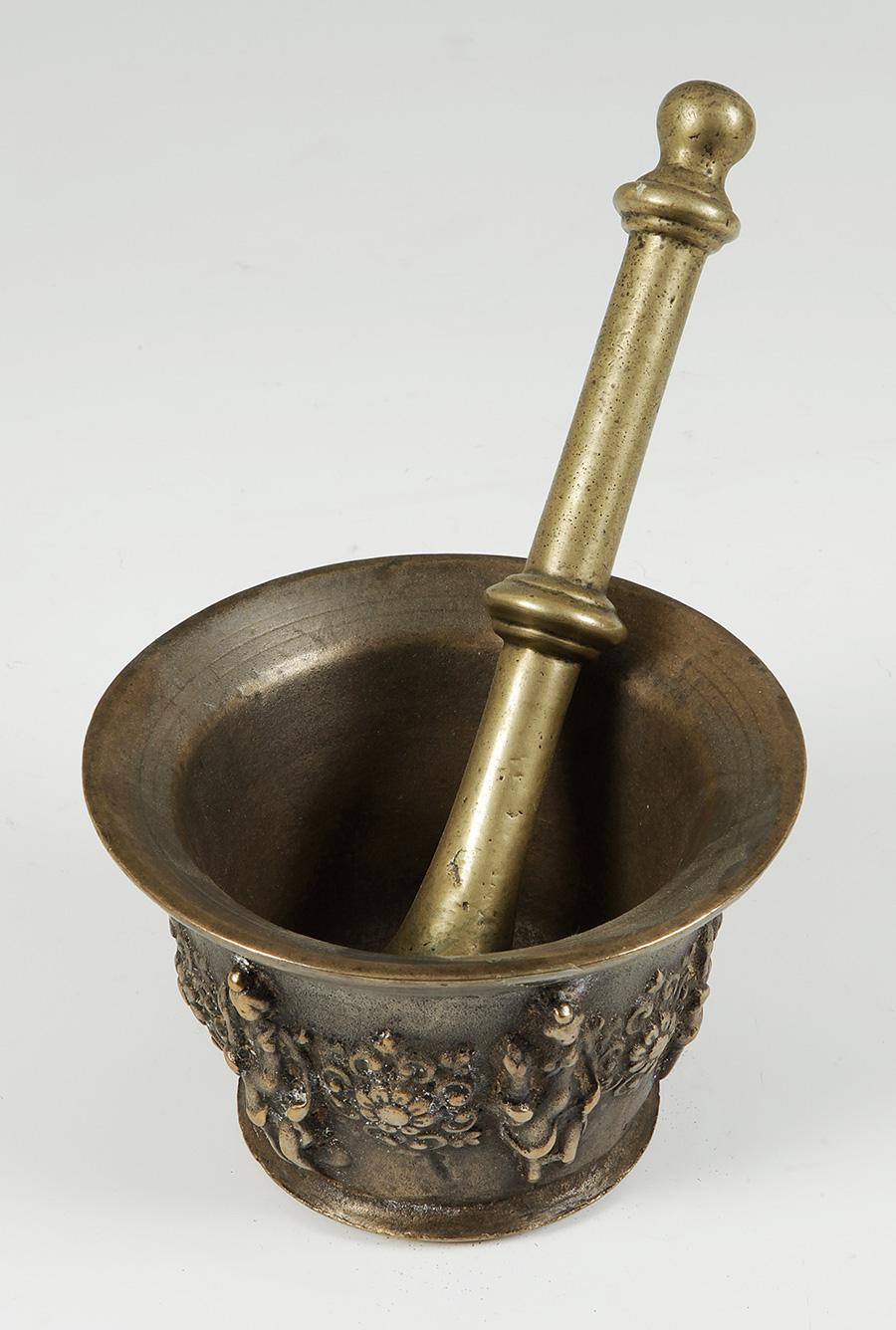 Mortar in bronze of Baroque epoch, with structure in the shape of inverted bell with circular flat base and open mouth. It is decorated with Classic female figures, alternated with rosettes bordered by tornapuntas, which fulfill the function of the