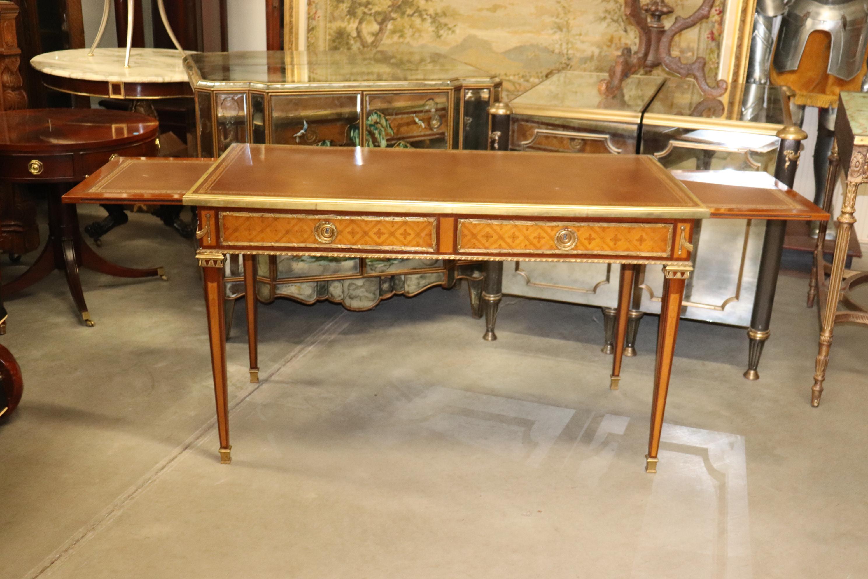 This is a superb French-made bronze mounted inlaid desk with bronze wrapping the top and brass and bronze ormolu everywhere. The desk is inlaid in tulipwood with a kingwood case. There are two leather top pull out slides that add an additional work