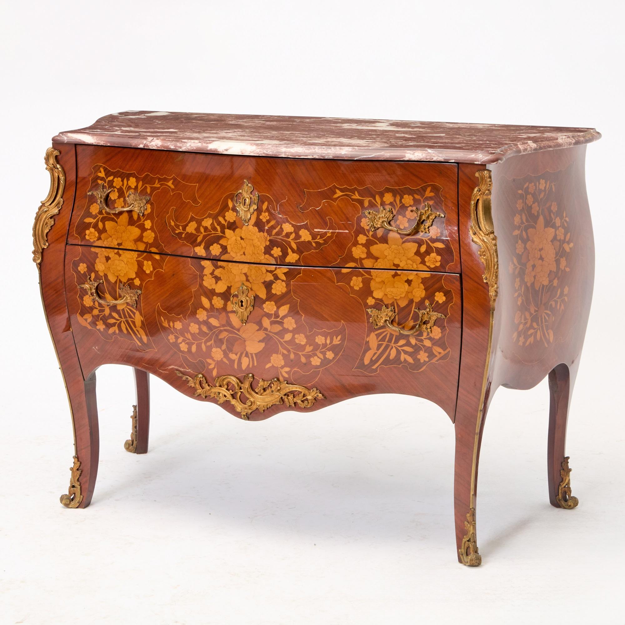 Questa squisita commode antica incarna l'eleganza dell'artigianato italiano della metà del XIX secolo, progettato nel sofisticato stile Luigi XV. Caratterizzato da una ricca impiallacciatura in legno di re, il pezzo è impreziosito da un intarsio