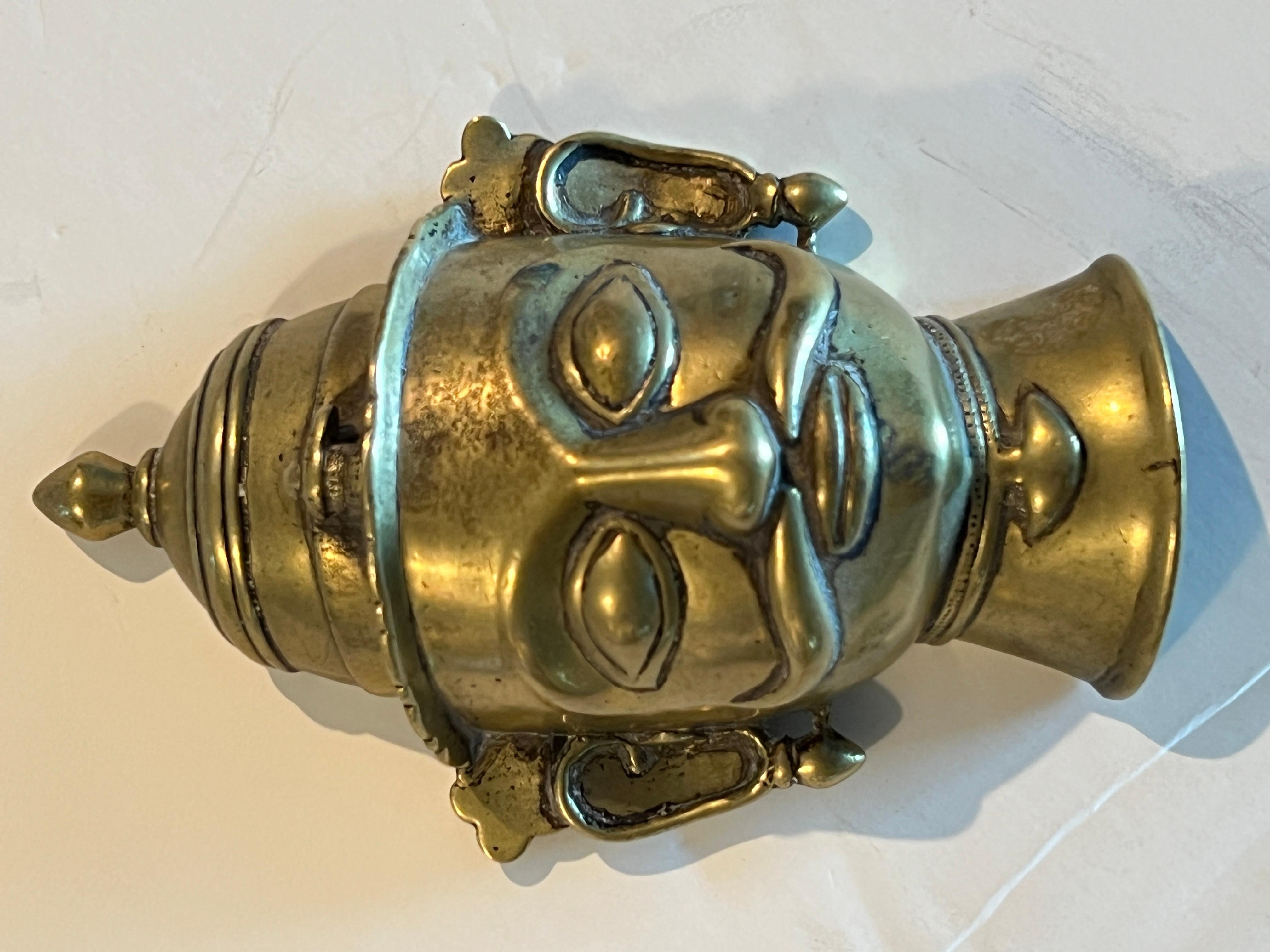 Questa placca di bronzo raffigurante Shiva con un volto umano era destinata a fungere da copertura del lingam.  Questo esemplare ha dei baffi elaborati,  un cappello a campana con una lampada a olio sull'orlo, occhi a mandorla, orecchini e una