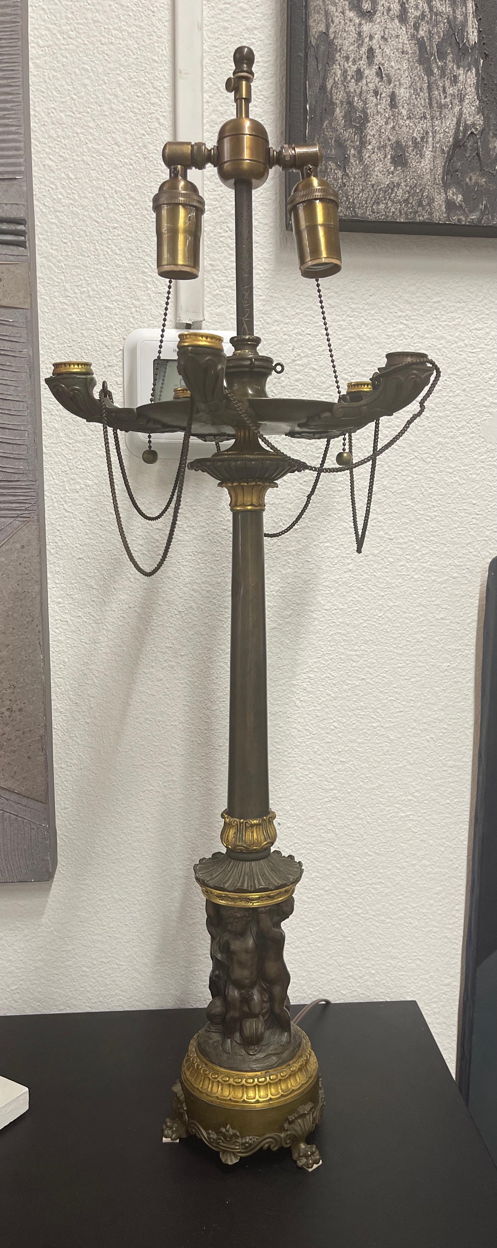 A lovely bronze neo classical lamp with cherubs adorning the base and faux oil lamp cups on top.  Exquisitely detailed casting details on this grand tour themed lamp. It has just been rewired and works well.  In good age appropriate condition with