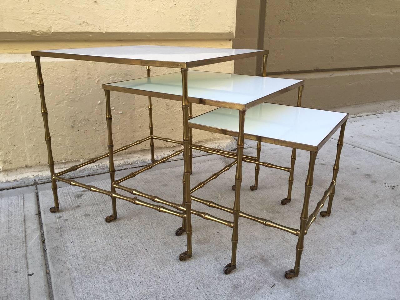 Bronze nesting tables by Maison Bague`s. Tables have bronze, faux bamboo frame on casters with milk glass tops.
Larger table measures: 19