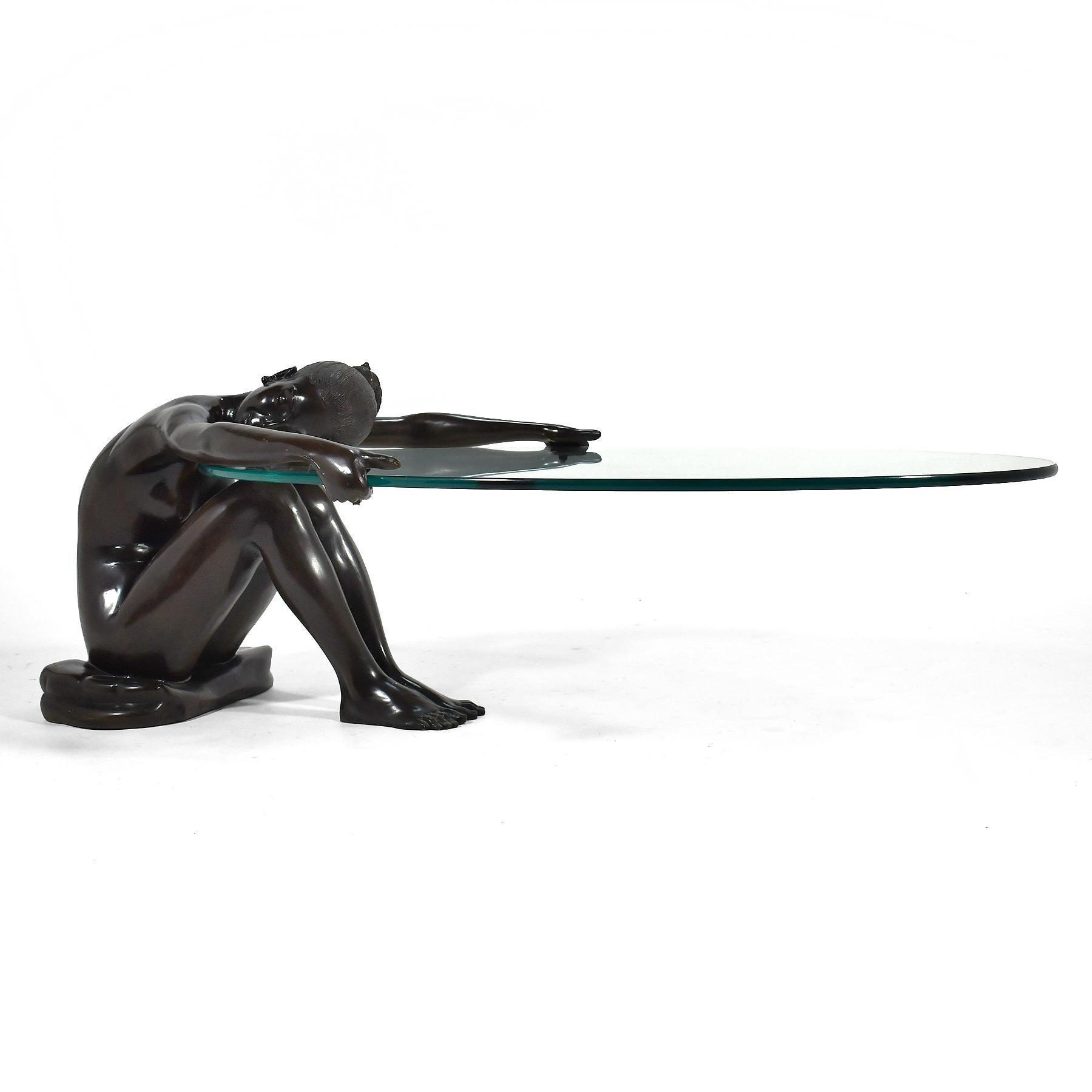 This dramatic coffee table has terrific presence in any room. The base is a bronze sculpture of a nude woman who sits, resting on a small pillow, as she reaches out and cradles the cantilevered glass top. We have seen other examples of this form,