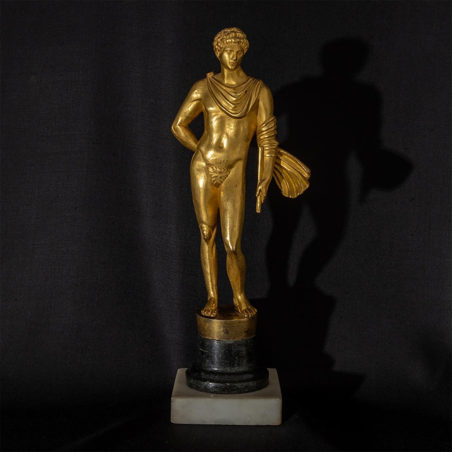 Gilt bronze of the Aetolian hero Meleager/Meleagros standing on a square marble plinth with a black round stone base. The cloak, strongly moved by the wind, wraps around his arm, in whose hand he still holds a lance broken in battle. After the