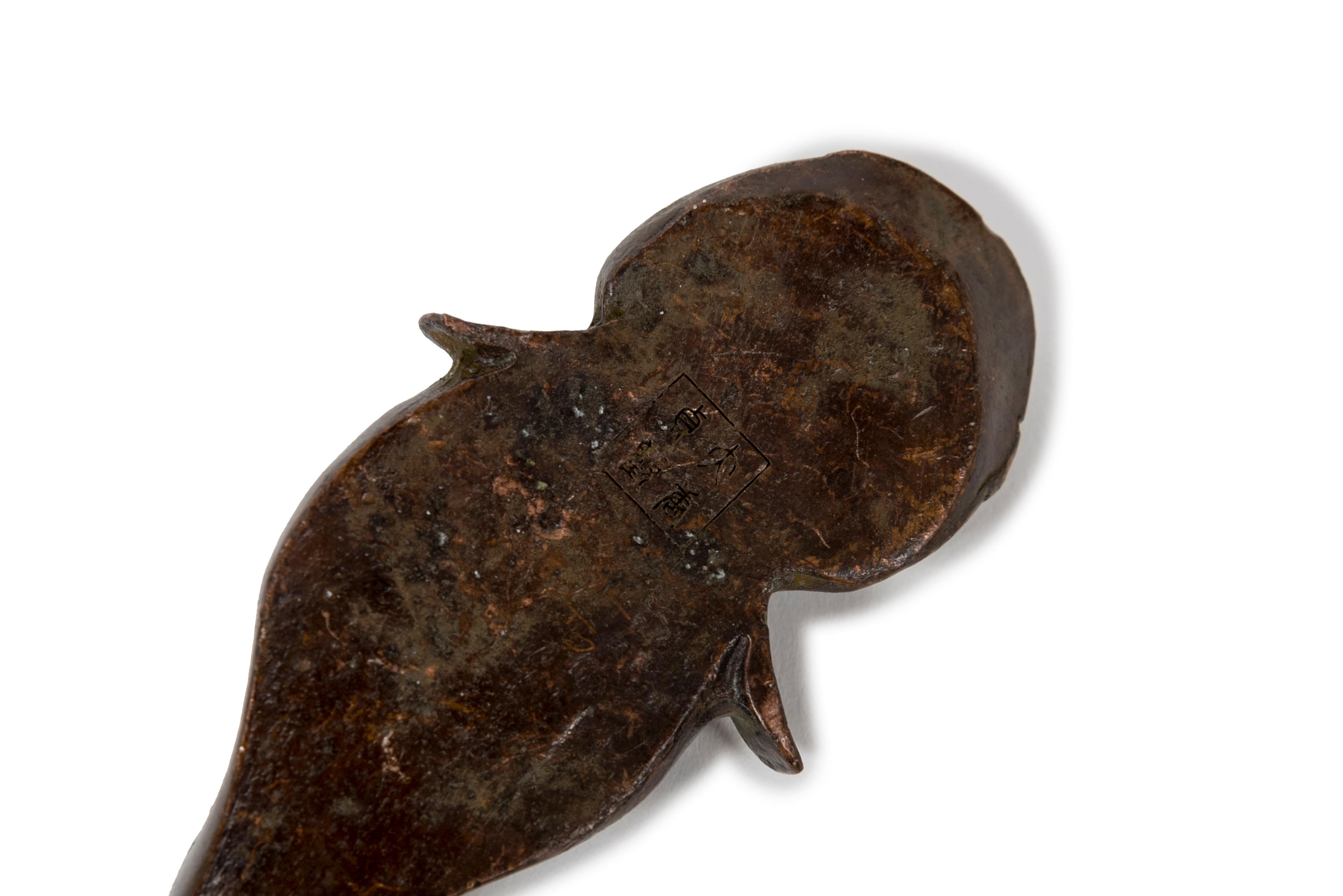 Skulptur oder Okimono aus Bronze eines gewellten Welses, der aus dem ruhigen Wasser auftaucht. Die Schuppen sind nicht dargestellt, und der Ausdruck von Augen und Mund könnte als naiv betrachtet werden. Eine andere interessante Deutung könnte sein,