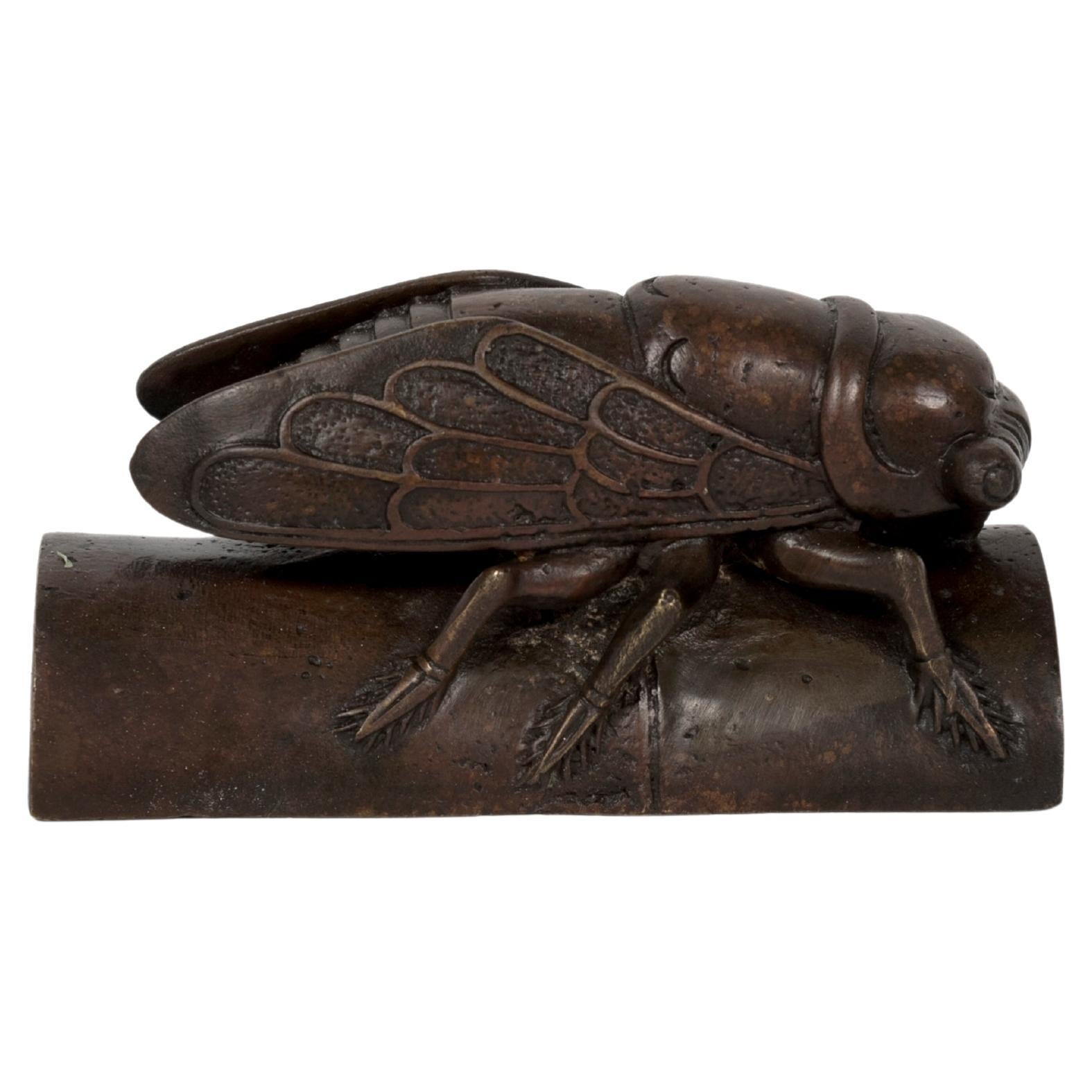 Escultura okimono de bronce de una enorme cigarra tumbada sobre un segmento de bambú