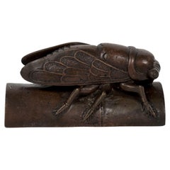 Escultura okimono de bronce de una enorme cigarra tumbada sobre un segmento de bambú