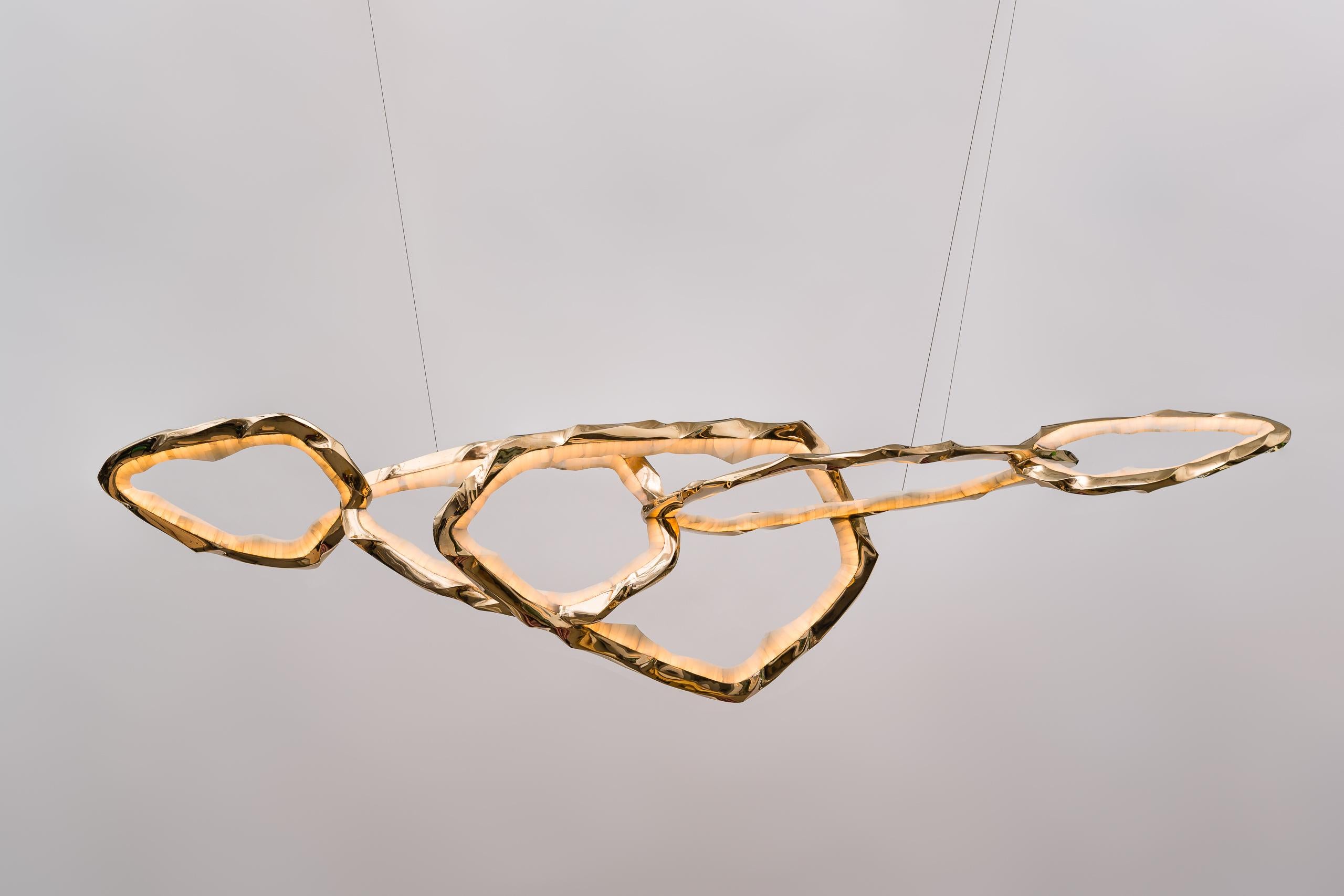 Composto da una serie di anelli di bronzo e onice collegati tra loro, l'ampio lampadario della serie Circlet di Markus Haase crea un ampio paesaggio di luce radiosa e scolpita. Combinando la padronanza delle tecniche di scultura tradizionali con un