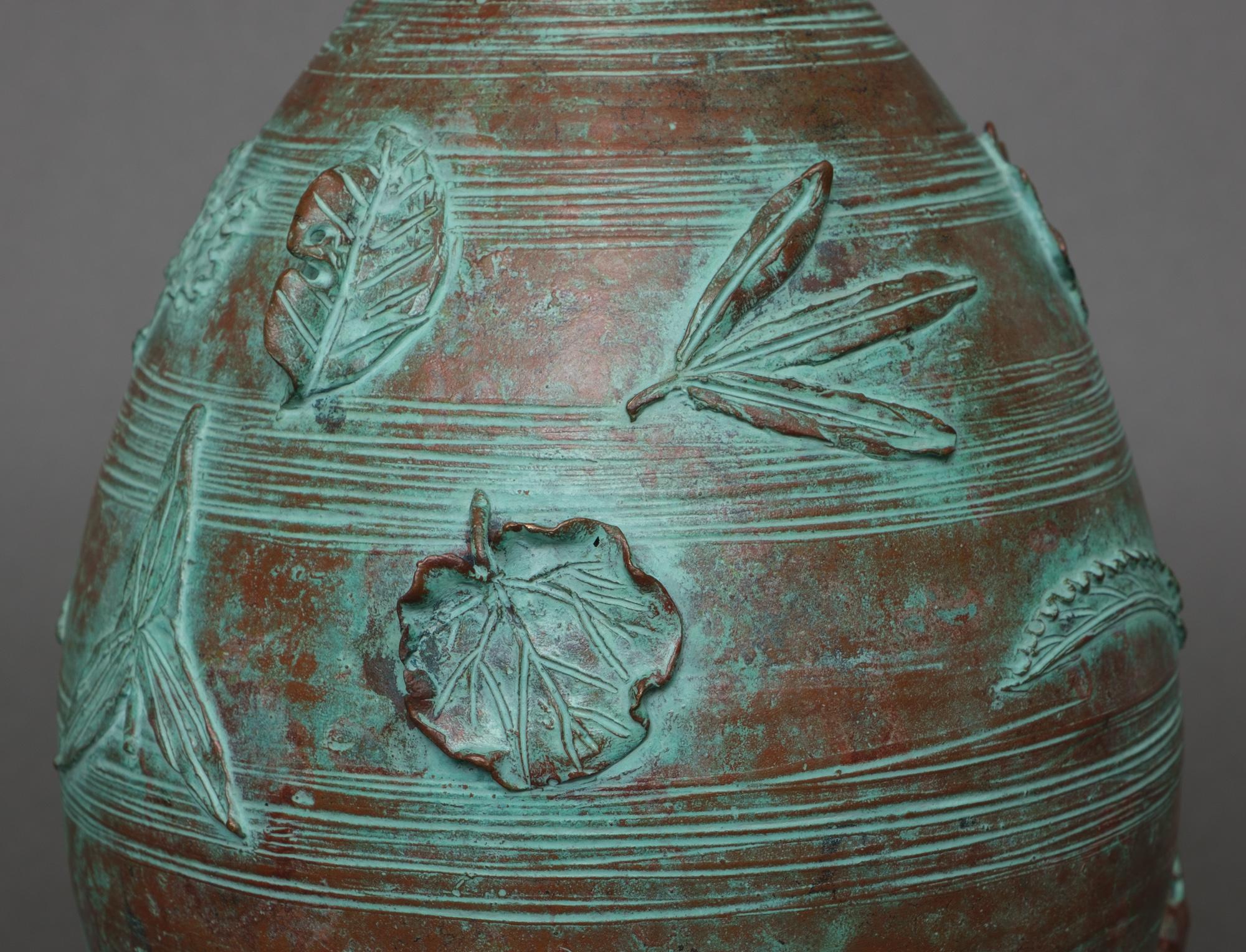 Beautiful bronze ovoid vase with a lovely icy green patina. Decorated with a continuous high relief design of all different kinds of leaves being swept around the vase by heavy gusts of wind. 

The lower edge signed and sealed by the artist Hirai