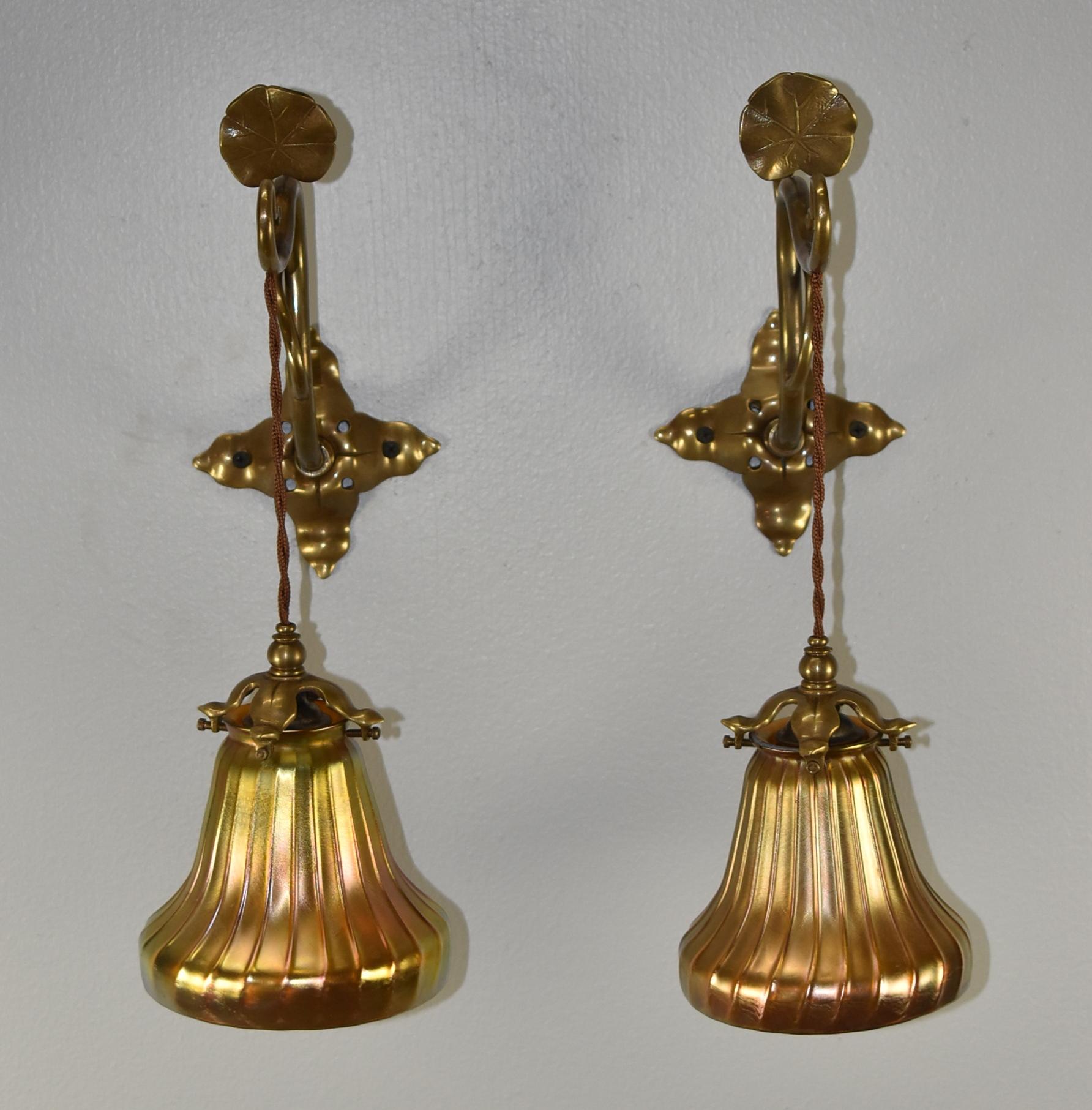 Pair bronze Art Nouveau style wall sconces with lily pad detail. Ribbed gold aurene art glass shades that measure 4.5 tall x 5