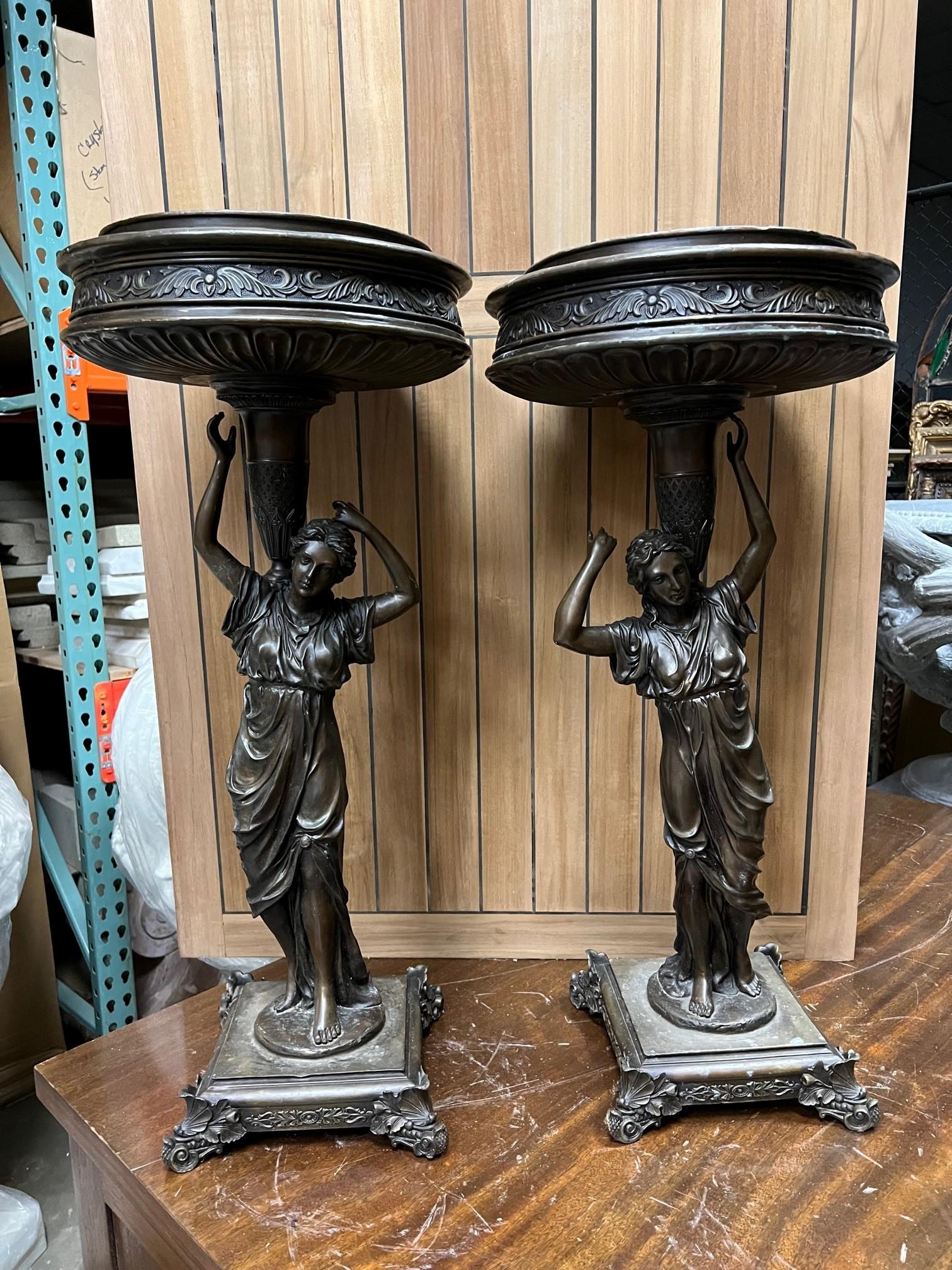 A Classical style bronze pair of figural urns of a woman holding the circular basin. I believe they were imported in from Thailand in the late 1990s early 2000. They are a pair but one is 31