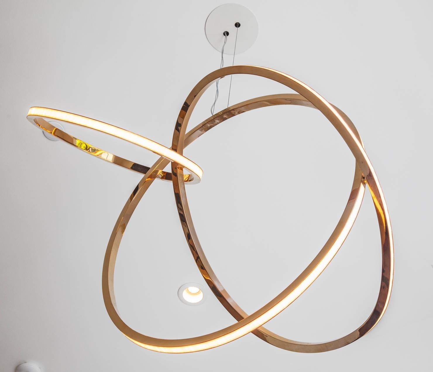 Niamh Barry’s Patera references the complex scalloped edges of shallow craters. The suspended light sculpture, illuminated by LED lights under glass opal tiles, features Barry’s signature floating hand-formed bronze rings. Barry’s dynamic,