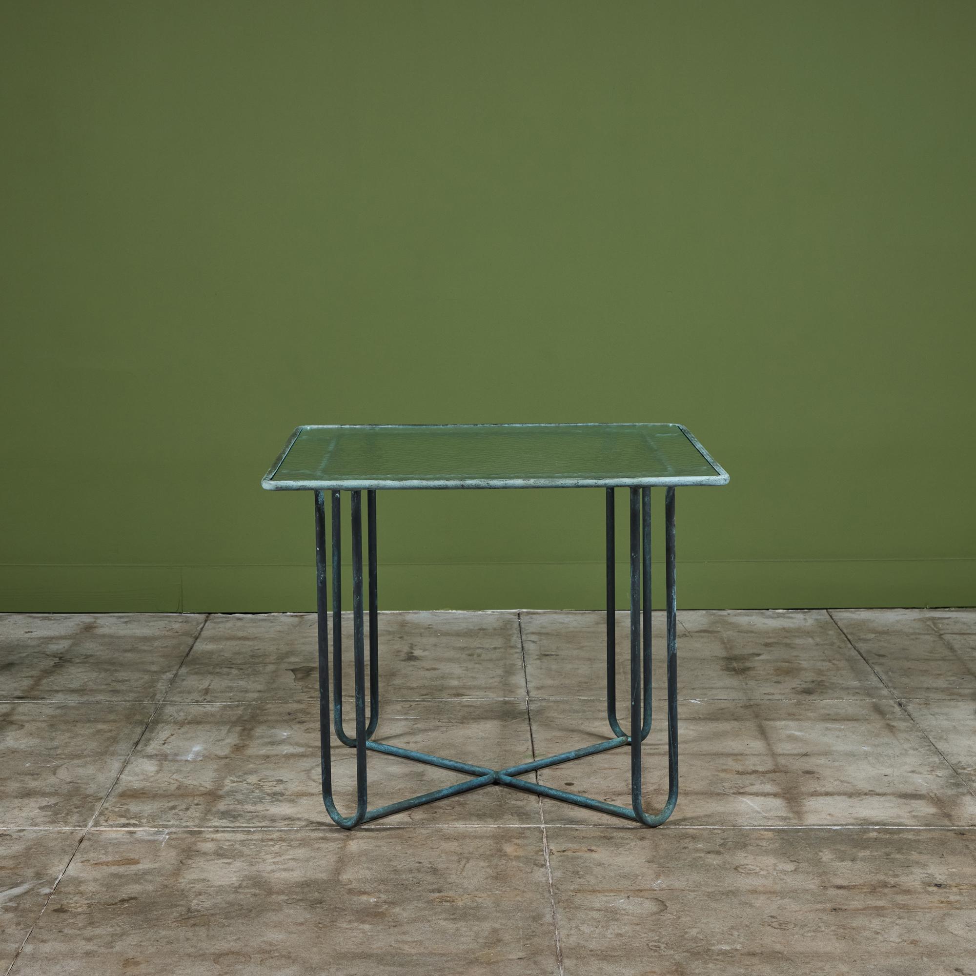 Pequeña mesa de comedor o de cartas de bronce patinado diseñada por Walter Lamb y fabricada por Brown Jordan. La mesa tiene forma cuadrada con esquinas redondeadas, y se apoya en cuatro patas de horquilla de bronce a juego. Las patas están unidas
