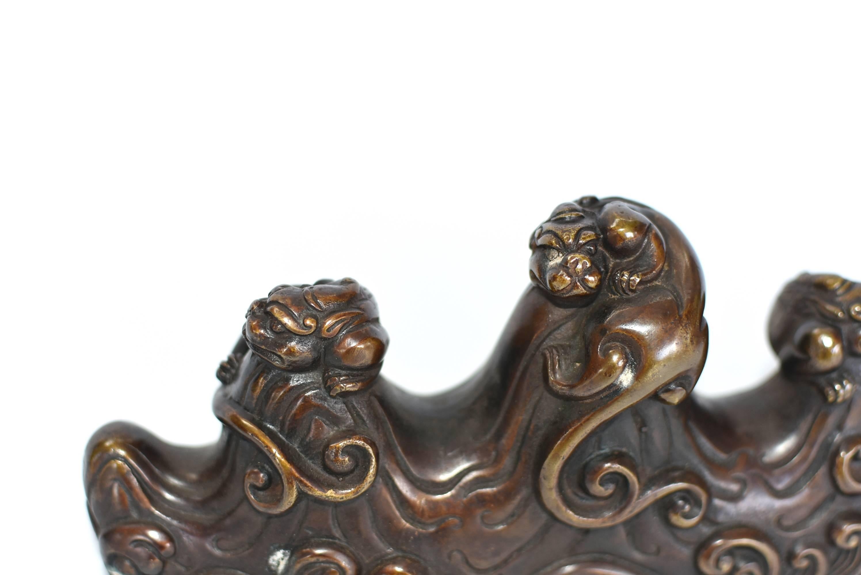 A beautiful Chinese bronze pen/brush rest. The bronze piece features three dragons perched on waves. Their tails blend into the waves, making an artistic statement. There are four slots to rest your pen or brush, each polished to perfection. The