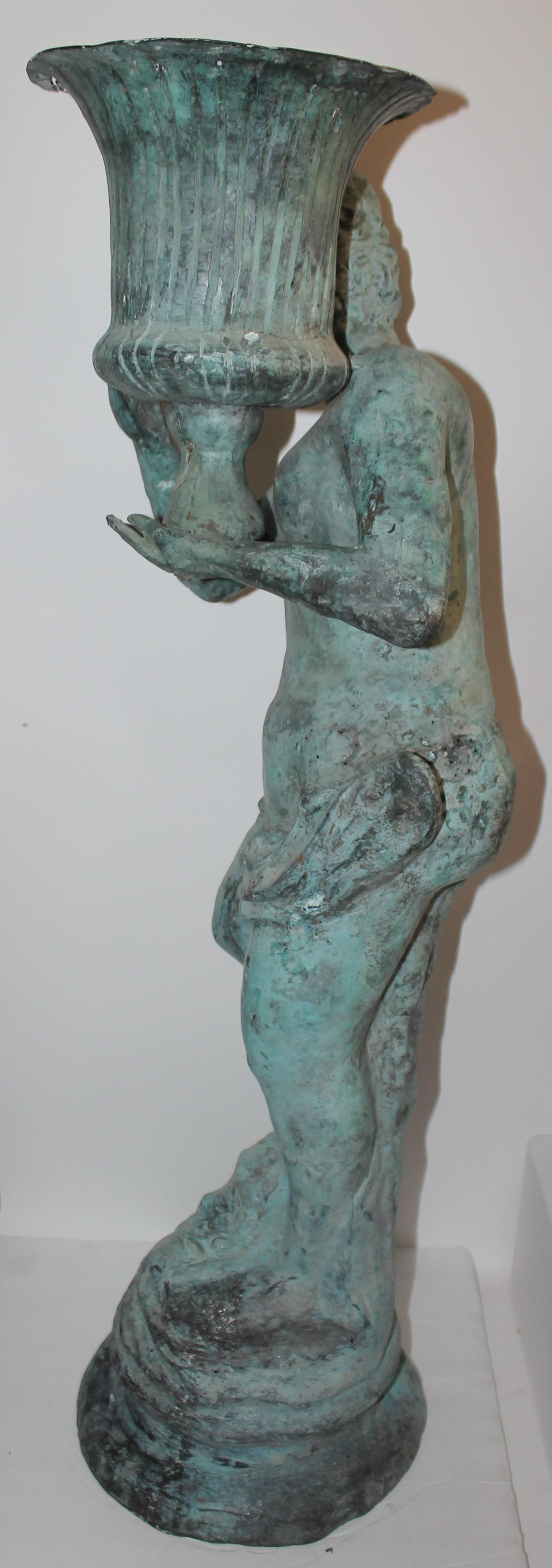 Bronze life sized statue of boy holding urn. 
There is a hole at the bottom that may be used as a water drain when being used as a garden planter. There is wear from age and use which has formed great patina. This item is in great condition. Circa