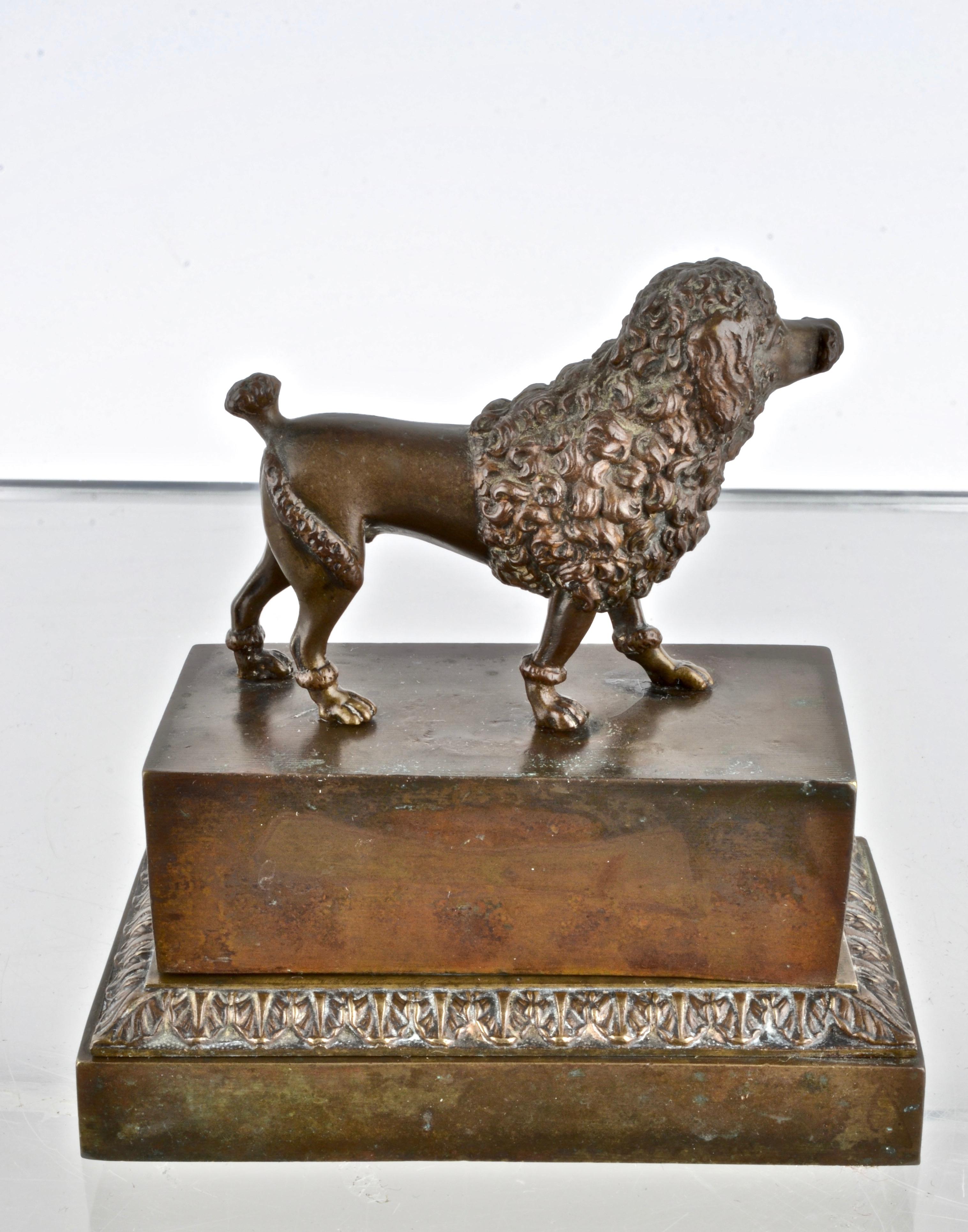 A detailed figure of a standard poodle stands on this antique inkwell. All bronze with wood bottom. Interior holes for inkwells. No inserts. Acanthus leaf detail around base. Finely cast. Antique patina.