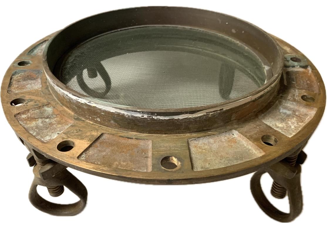 Vintage bronze porthole with mesh screen and four dogs, 3 bolts and a brushed nickel or aluminum flat flange. Maker's name stamped into porthole.

Dimensions: 14