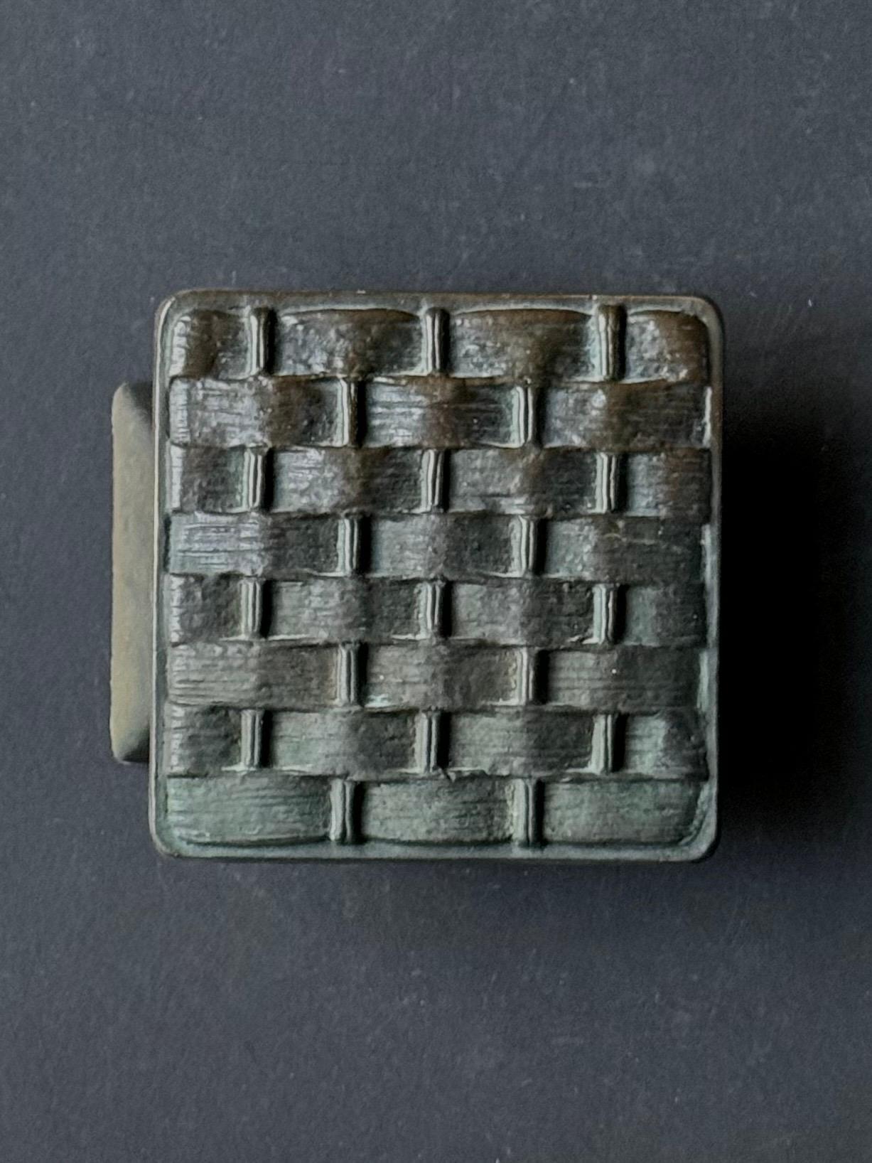 A square bronze push-pull door handle with a dark brown patina and raised basket-work pattern. Mid-to-late 20th century, European.

This is a heavy piece, made of cast and patinated bronze. We have not cleaned or polished the metal and it is offered