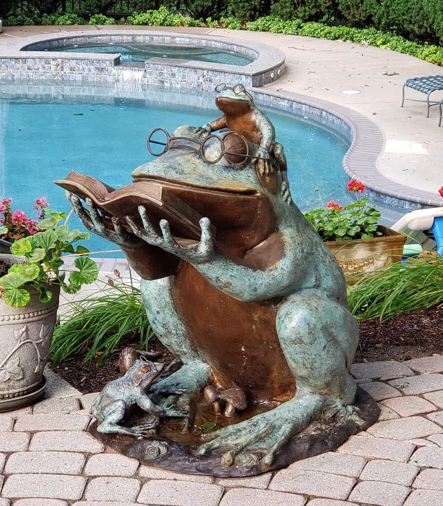 This lost-wax bronze frog statue showcased in our vast animals collection features a large frog sitting with an open book in his hands. While reading, one baby frog sits on top of the large frog's head looking on at the book while another baby frog