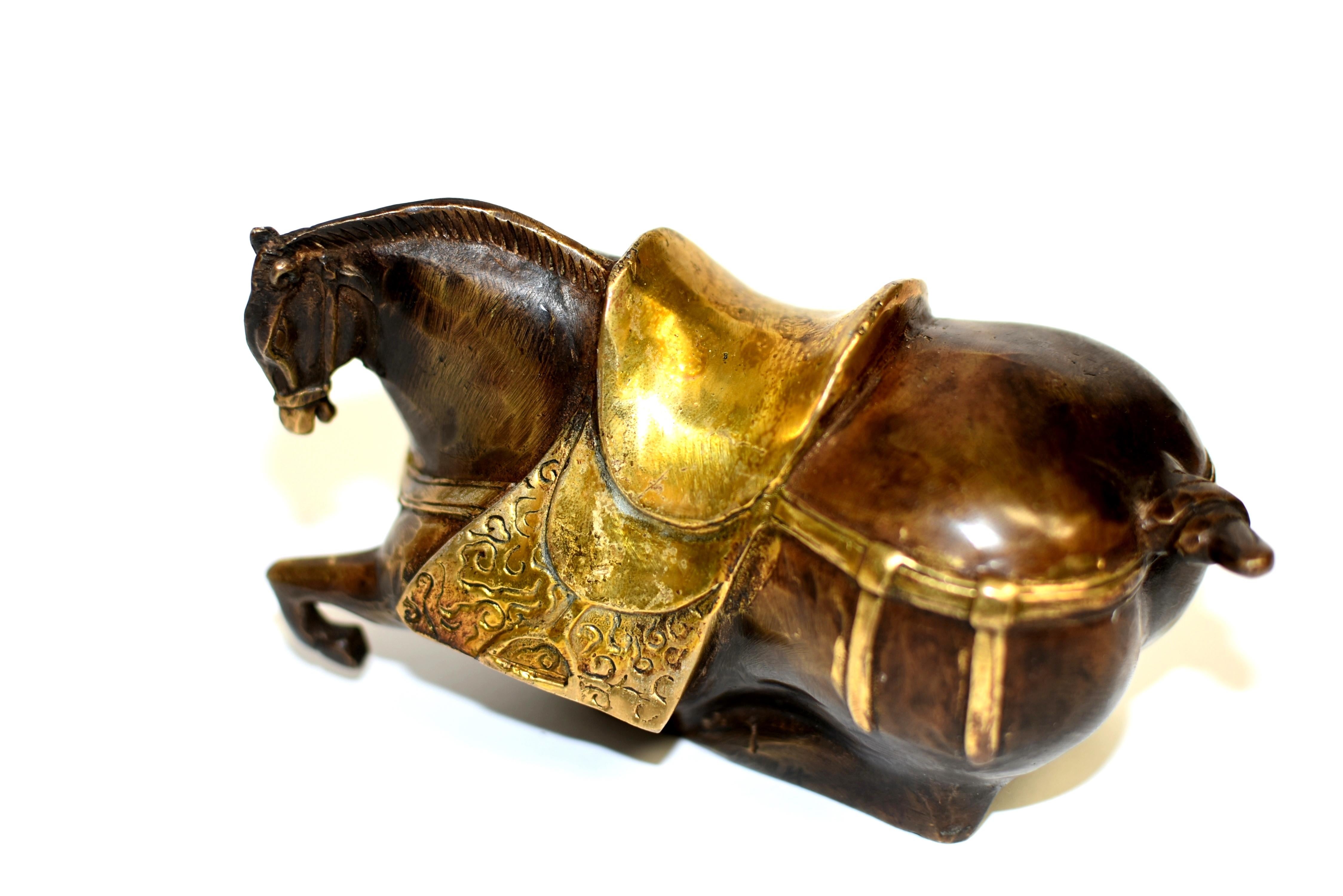 Cheval couché en bronze du XXe siècle, de style dynastie Han, dont les trois pattes sont repliées sous le corps et la tête légèrement tournée. La crinière bien incisée se rassemble proprement en formant une ligne de crête sur son dos, derrière les