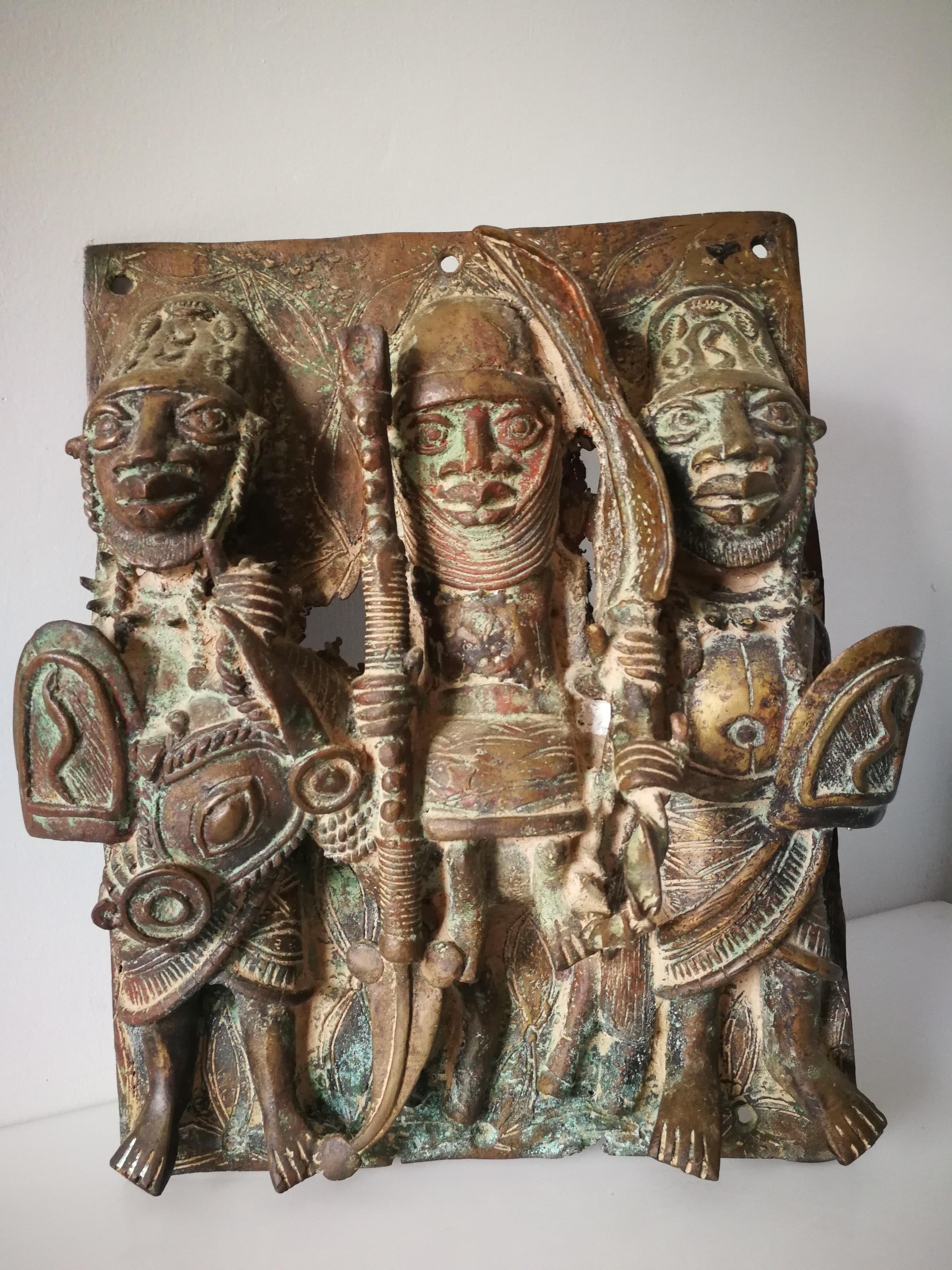 King with two members of the tribe - is a bronze relief sculpture of the tribe from the Nigeria-Benin area. It depicts three figures: tribesmen on the left and right holding shields, and the king in the center. Riding a horse and holding the royal