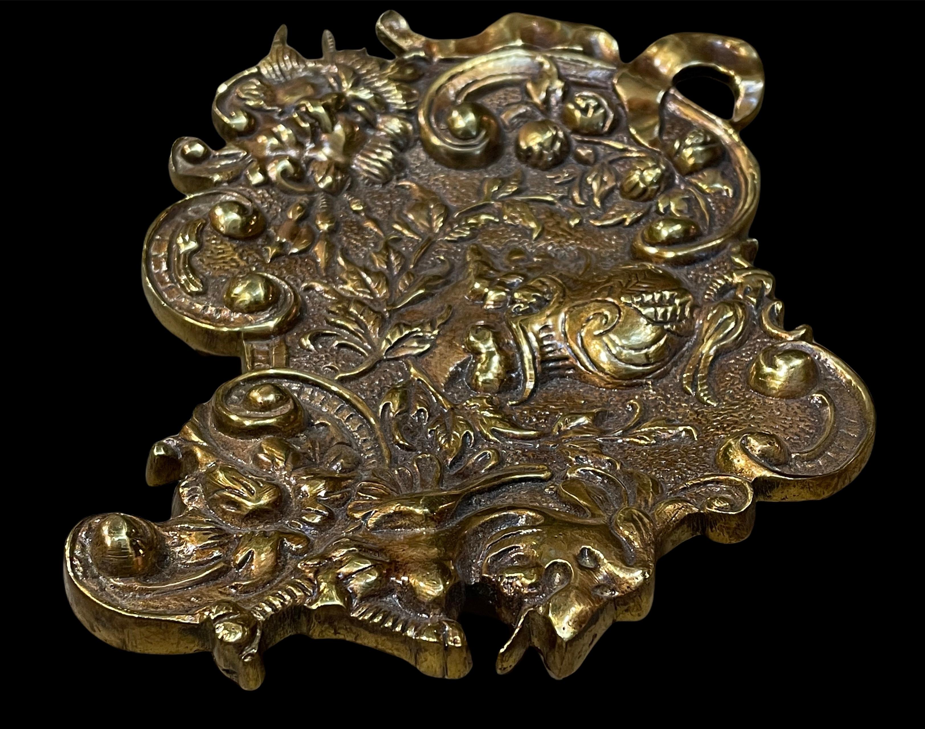 This is a rococo style bronze asymmetrical ring dish or pen rest. It depicts a repousse profile of a Roman warrior in the center. Around it, there are some C-scrolls of rocailles, foliages and ribbons. The dish stands in four small cylindrical